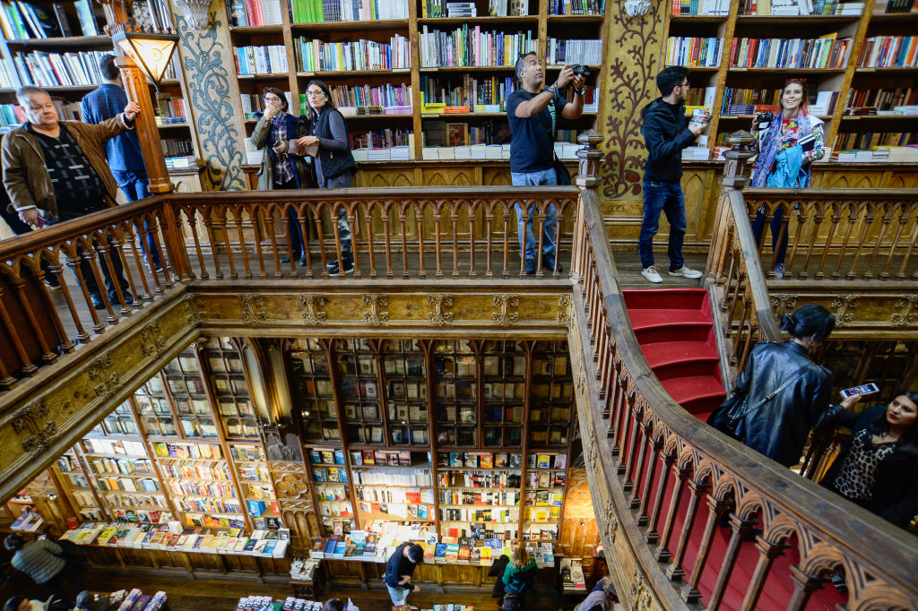 People browsing two levels of a bookstore filled with shelves of books, with some taking photos