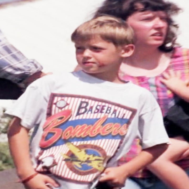 A young boy wears a "Baseball Bombers" T-shirt, standing next to a woman, likely a family member, who is holding a child