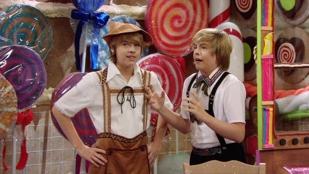 Dylan Sprouse and Cole Sprouse wear themed outfits resembling traditional German attire in a candy shop scene
