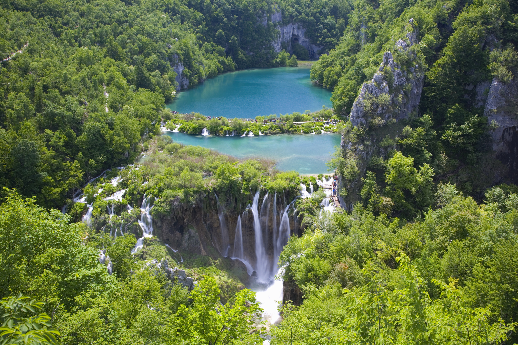 Aerial view of a lush green landscape featuring cascading waterfalls flowing into clear blue lakes surrounded by dense vegetation at Plitvice Lakes National Park