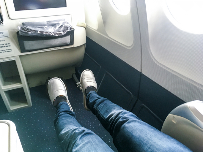 Person wearing jeans and slippers stretching their legs in an airplane's first-class cabin