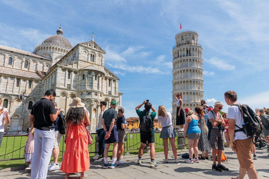 Tourists, including families and individuals, gather near the Leaning Tower of Pisa, some taking photos and admiring the historic landmark