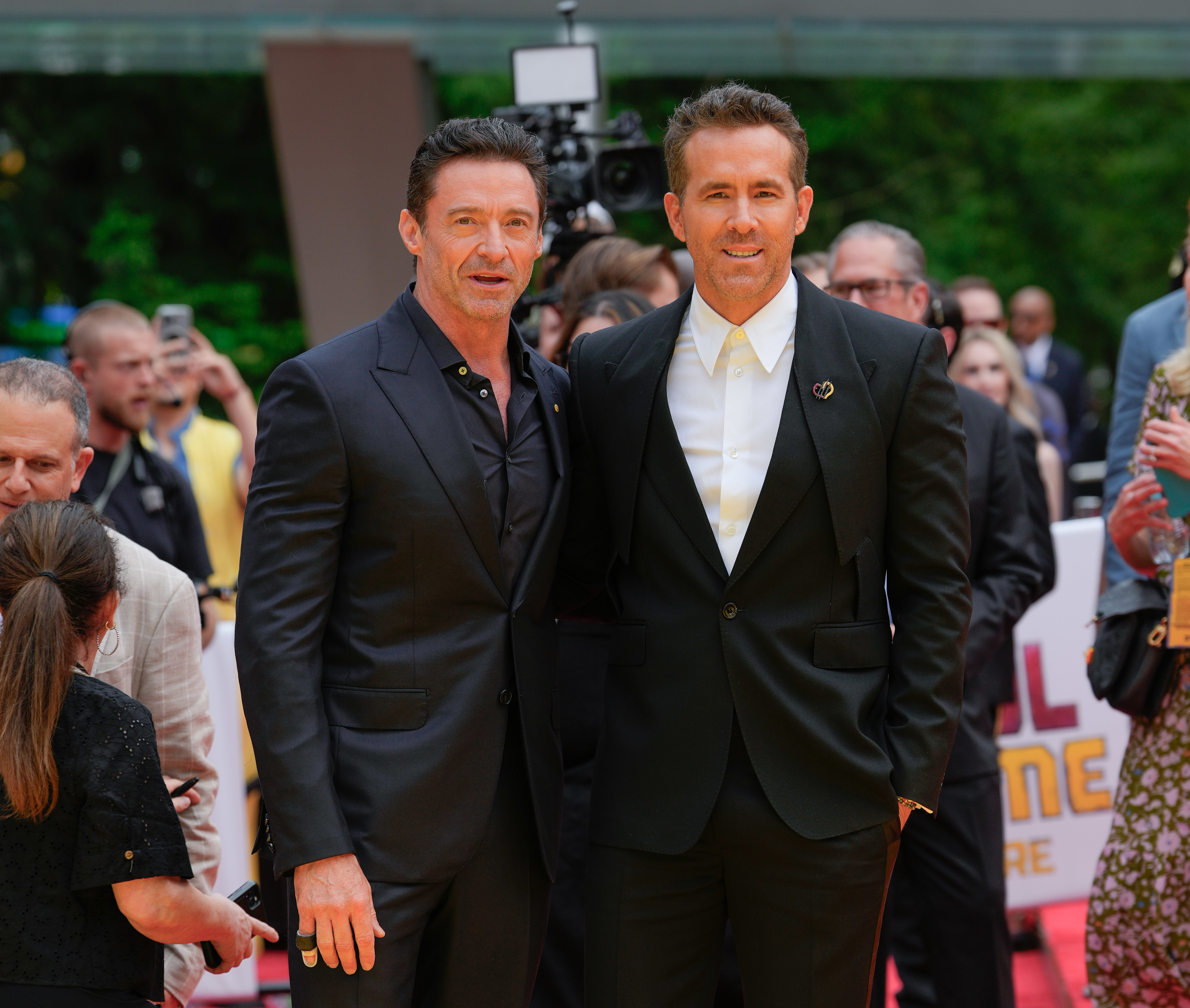 Hugh Jackman in a black suit and Ryan Reynolds in a dark suit with a white shirt, posing on a red carpet event