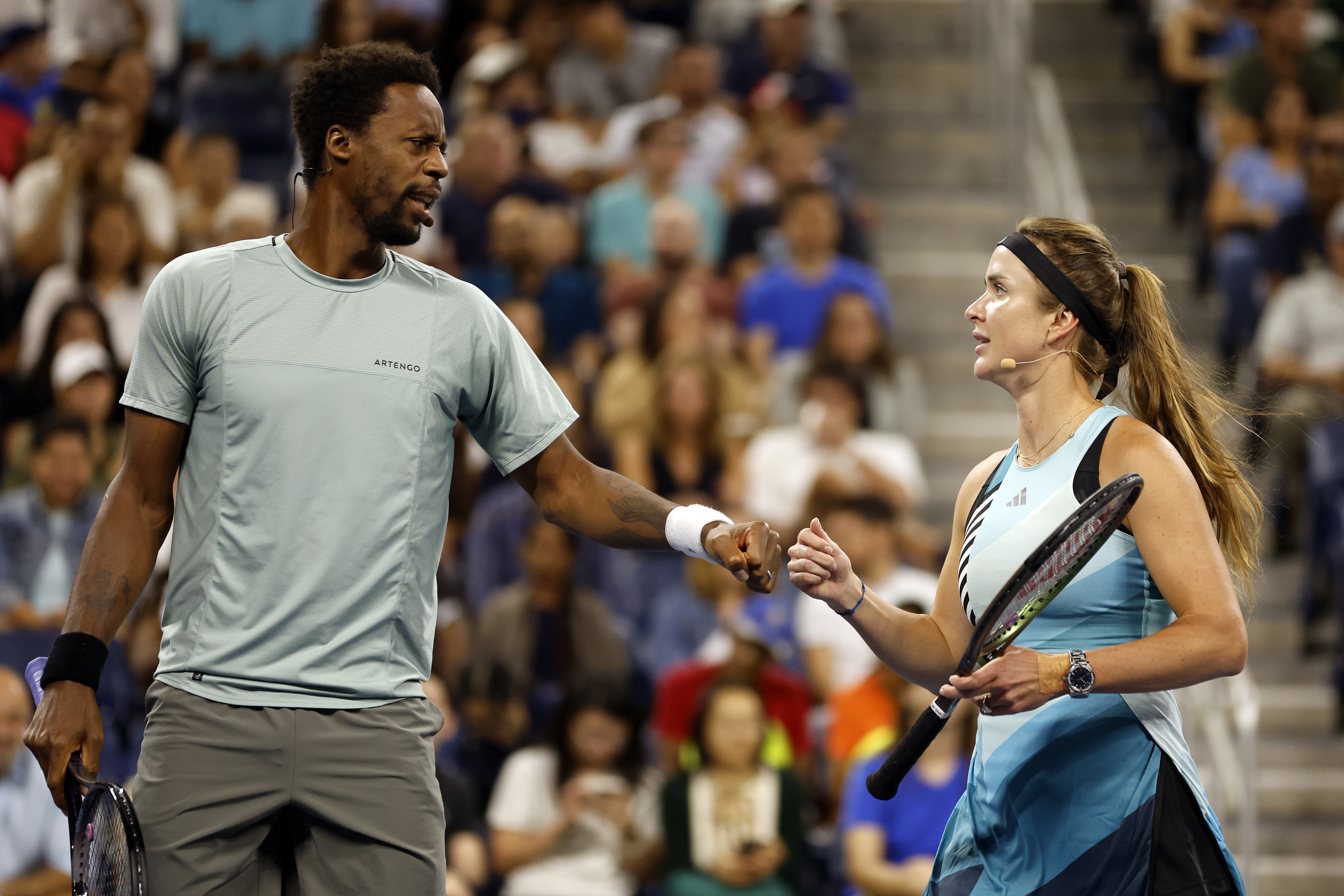 Gaël Monfils and Elina Svitolina shaking hands on a tennis court, both holding rackets, while spectators watch in the background