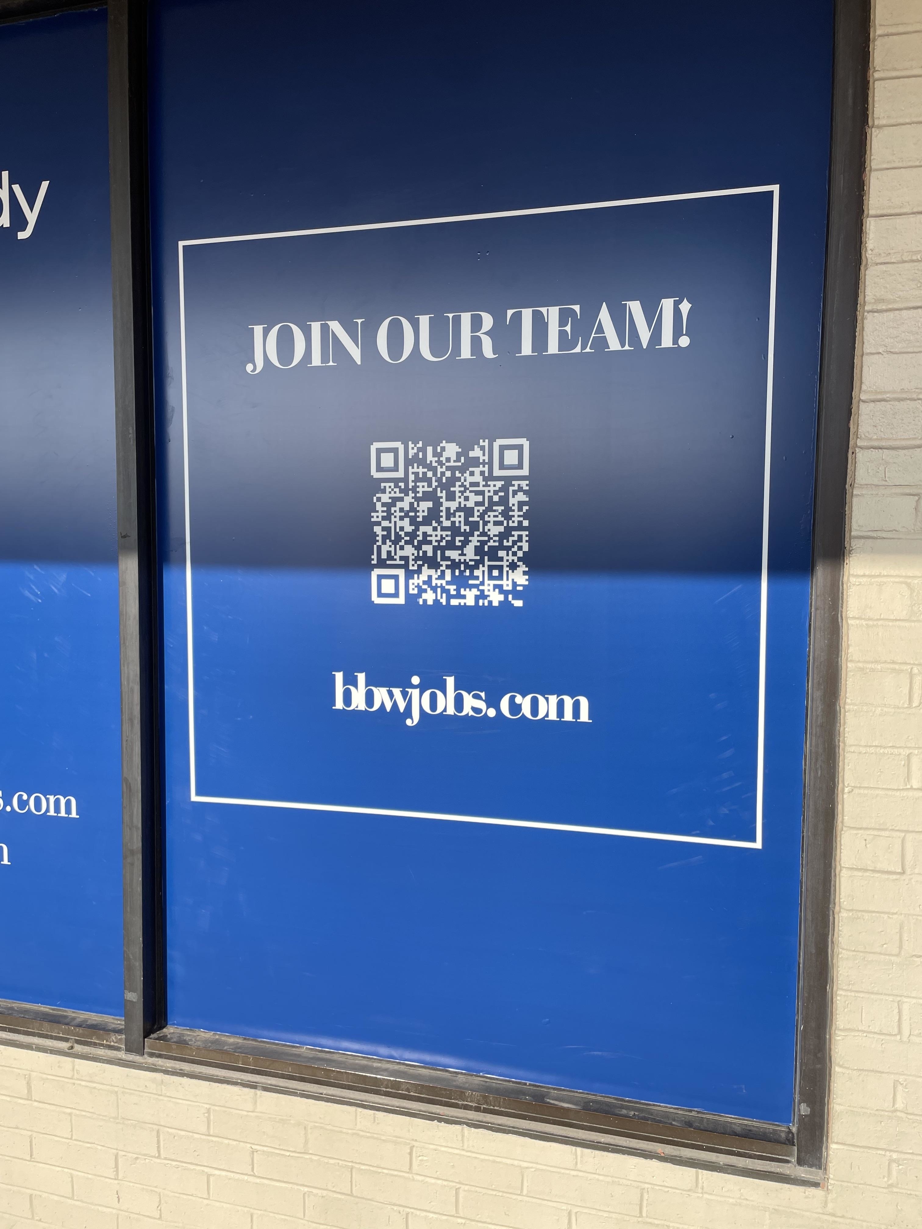 A sign with a QR code reading "Join Our Team!" and a URL "bbwjobs.com" is displayed on a window