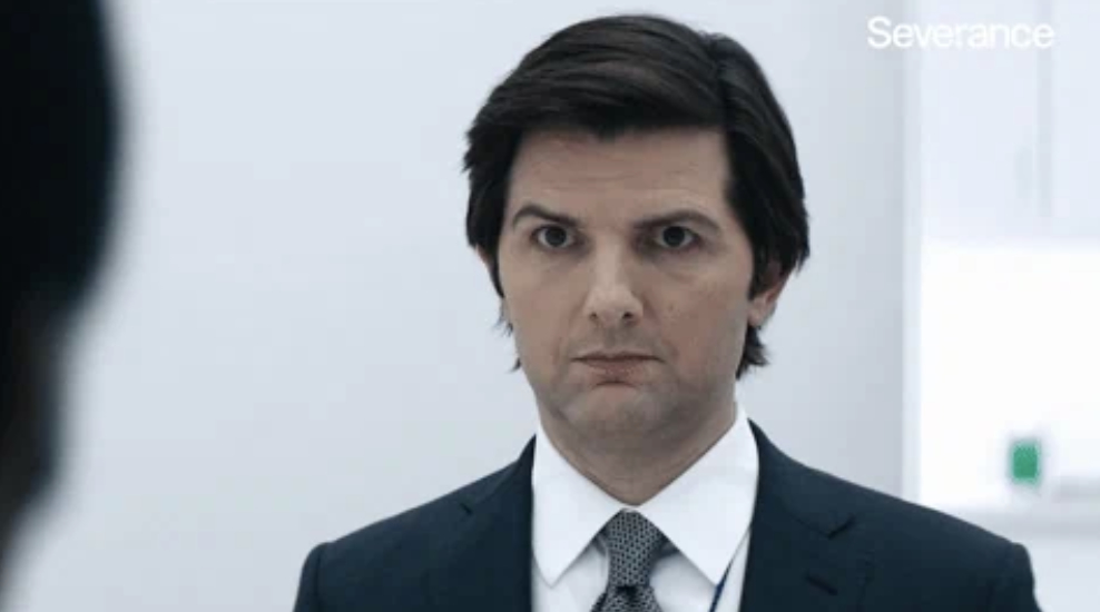 Adam Scott, in a suit and tie, with a serious expression, from the TV show &quot;Severance.&quot;