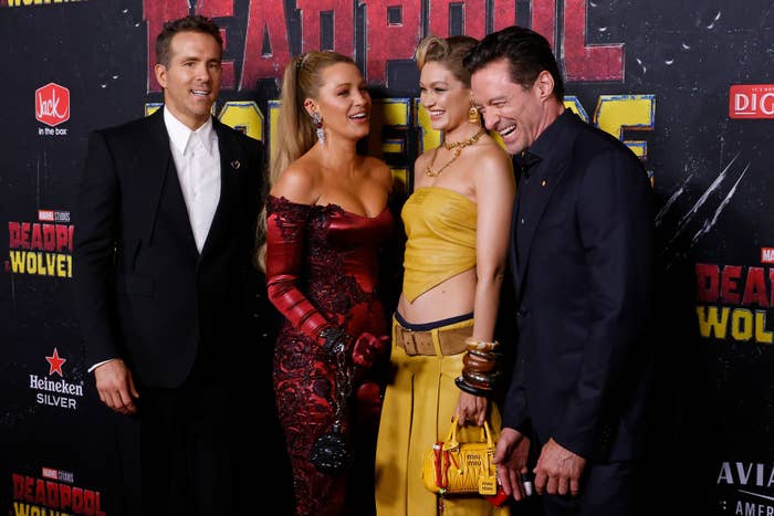 Ryan Reynolds, Blake Lively, Gigi Hadid, and Hugh Jackman at a red carpet event. Reynolds in a suit, Lively in an off-shoulder dress, Hadid in a crop top, Jackman in a suit