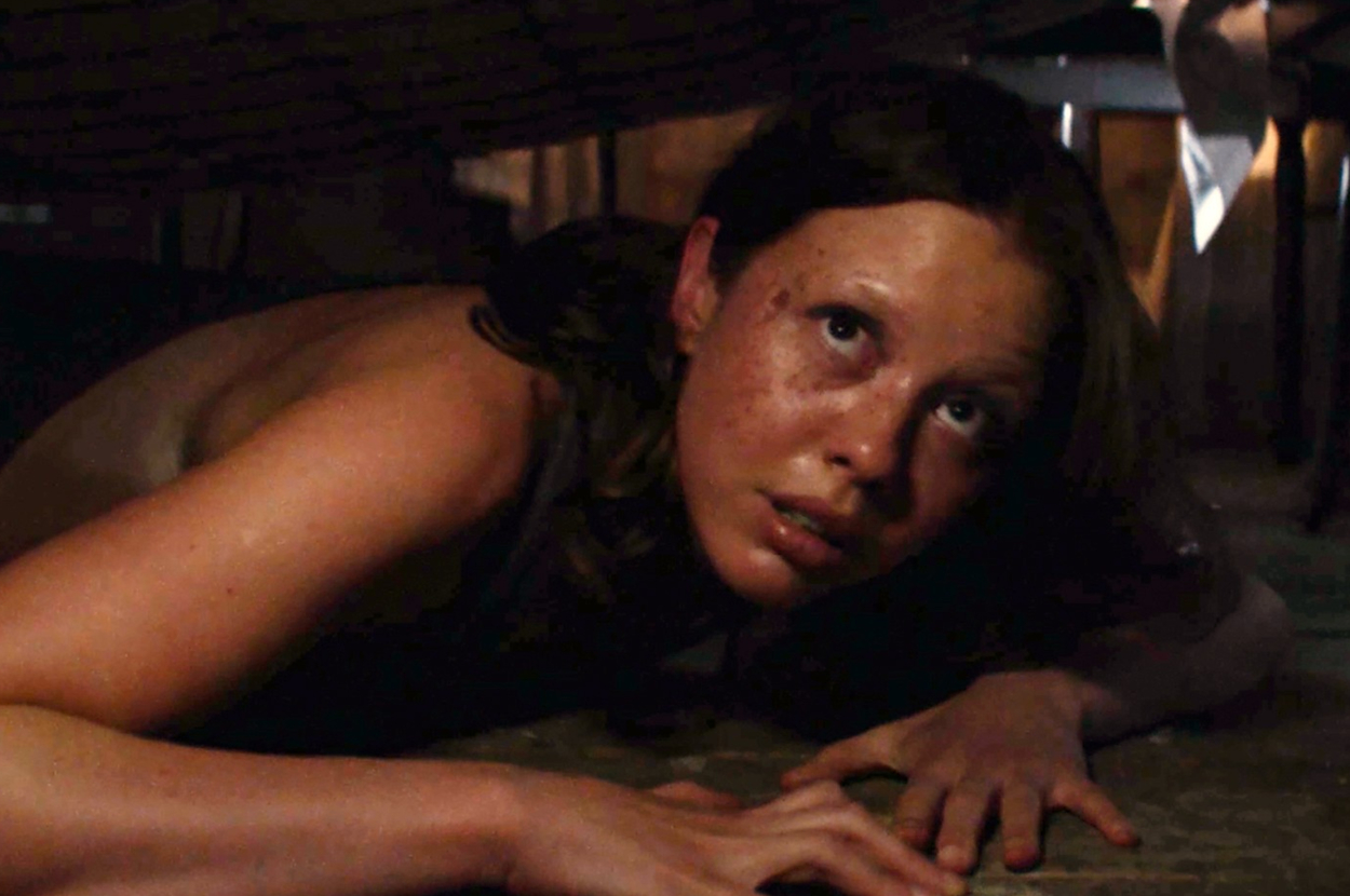 Mia Goth with freckles and long hair looks up anxiously while crawling under a surface