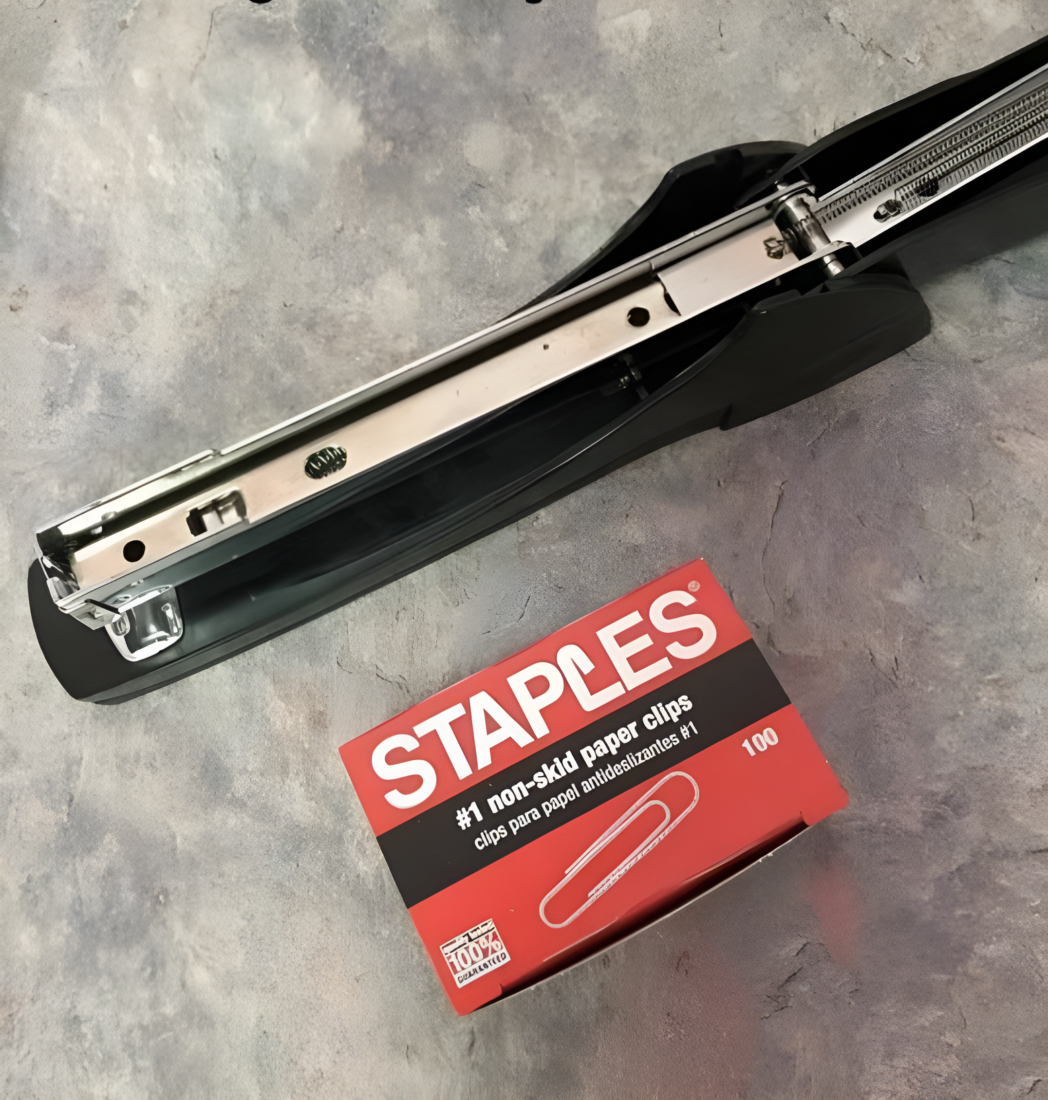 A heavy-duty black stapler next to an open box of Staples #1 non-skid paper clips with 100 clips