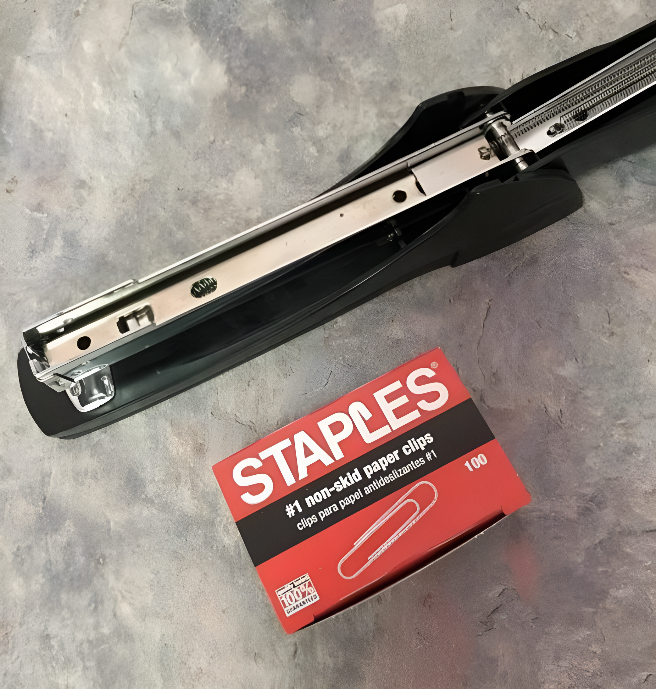 A heavy-duty black stapler next to an open box of Staples #1 non-skid paper clips with 100 clips