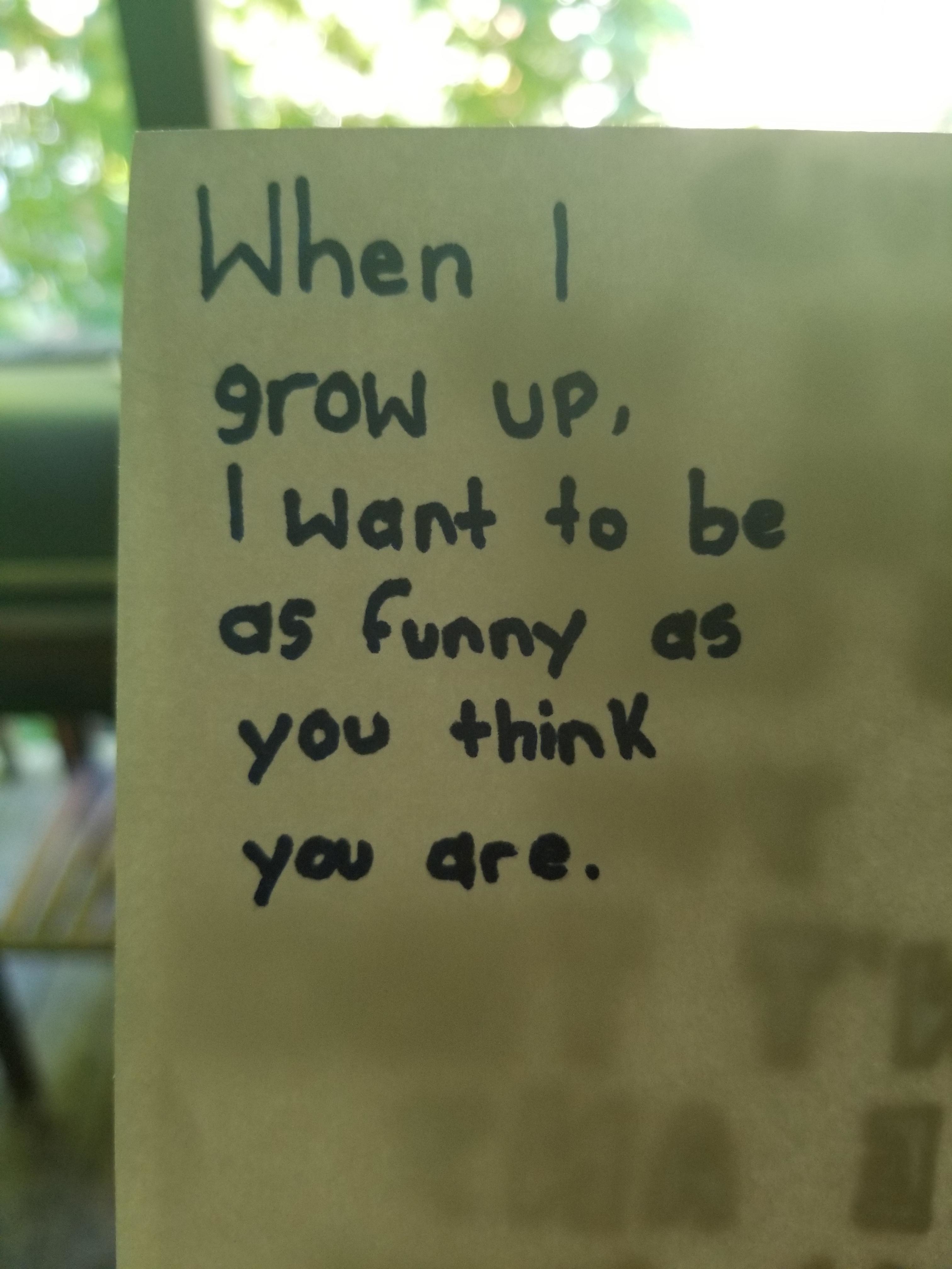 Handwritten note reads: "When I grow up, I want to be as funny as you think you are." The background shows a blurry outdoor scene