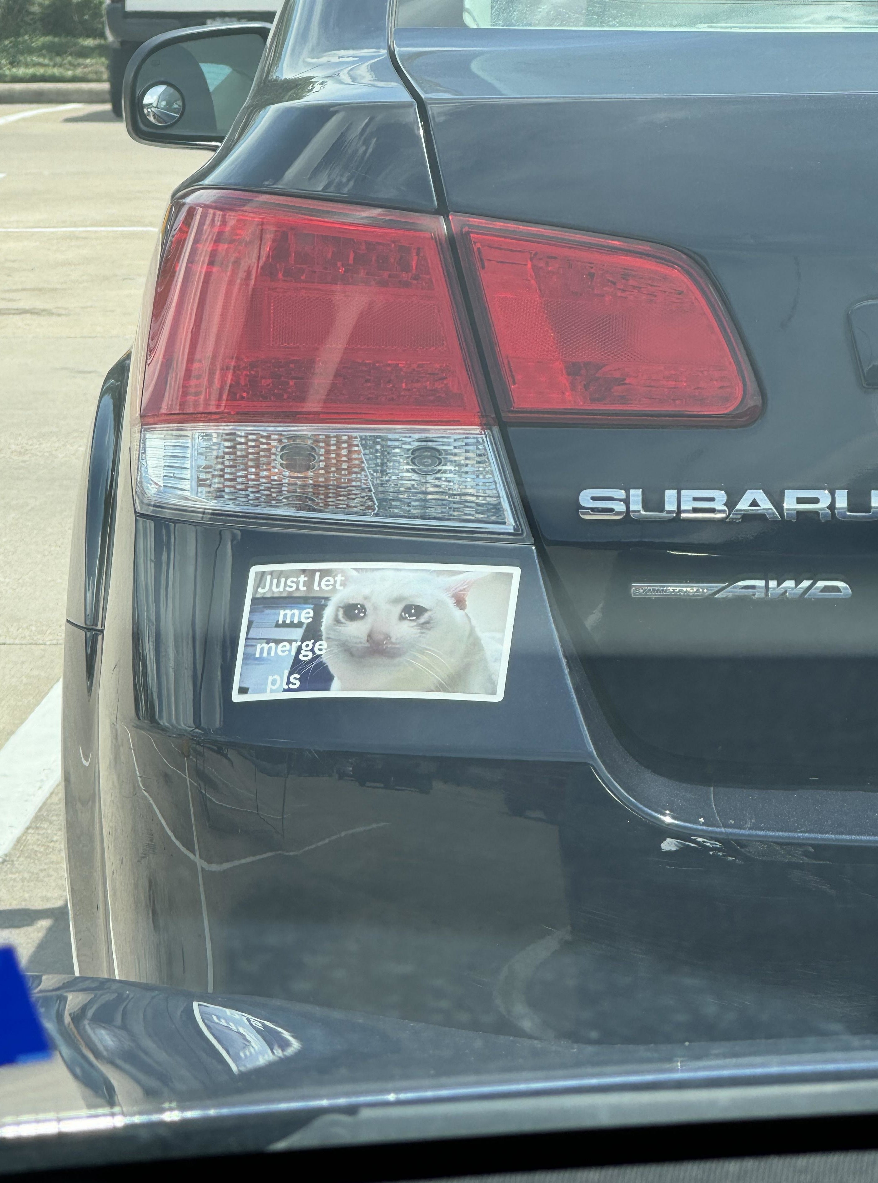 Bumper sticker on a Subaru car displaying a meme image of a grumpy-looking white cat with the text "Just let me merge pls."