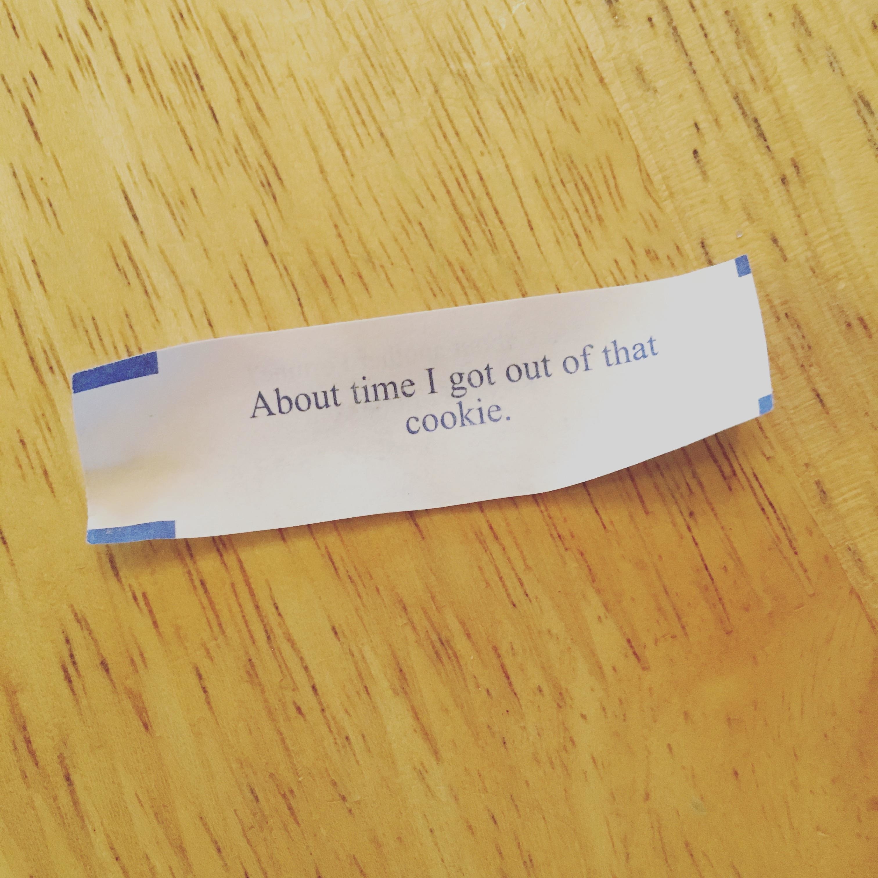 Fortune cookie message on a wooden surface reads, &quot;About time I got out of that cookie.&quot;