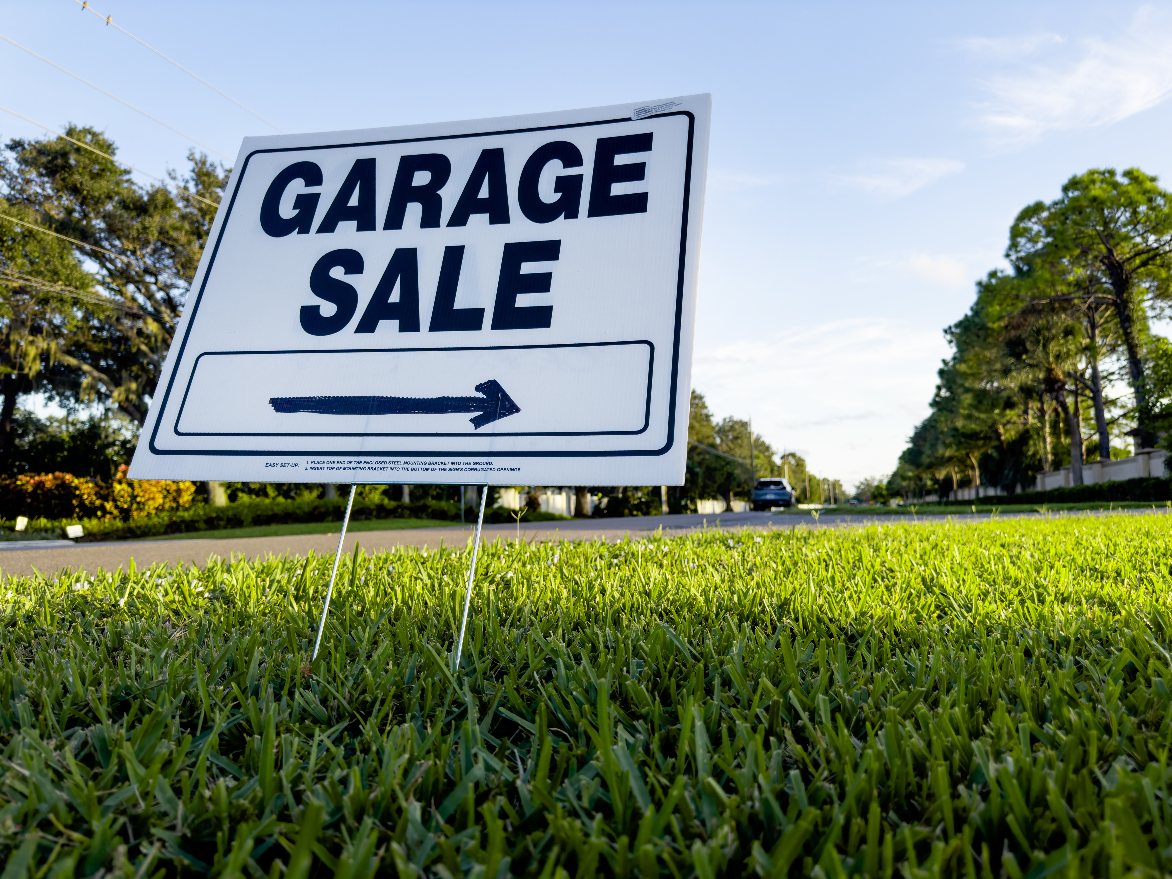 Garage sale sign with an arrow pointing to the left, placed on a lawn near a road