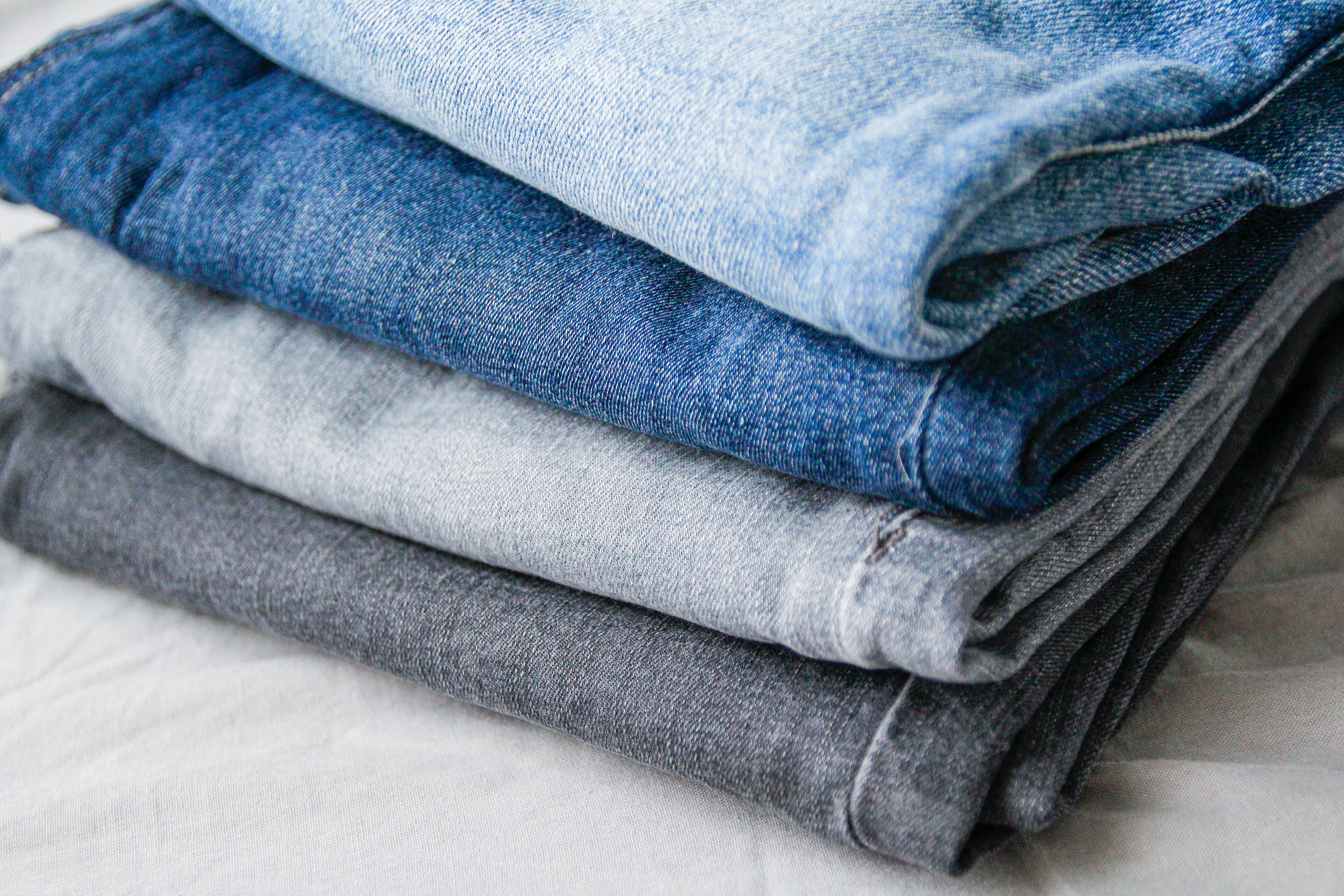 Folded stack of jeans in varying shades of blue and gray on a white surface