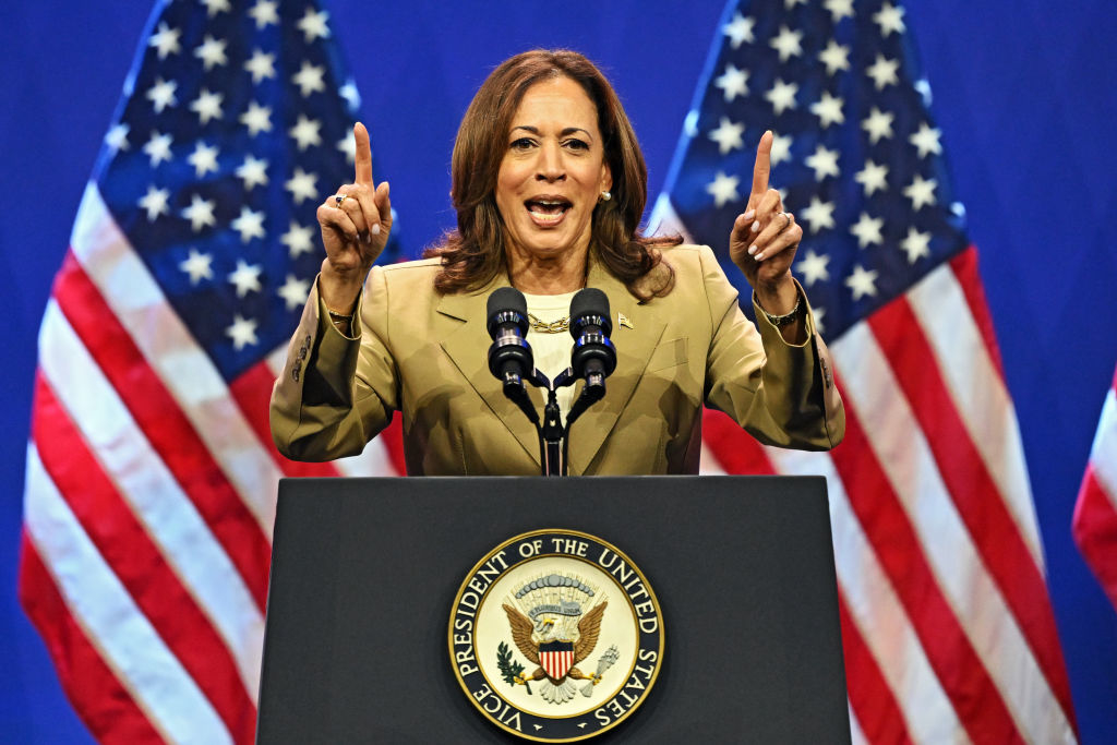 Kamala Harris speaking passionately at a podium with the U.S. presidential seal, flanked by American flags