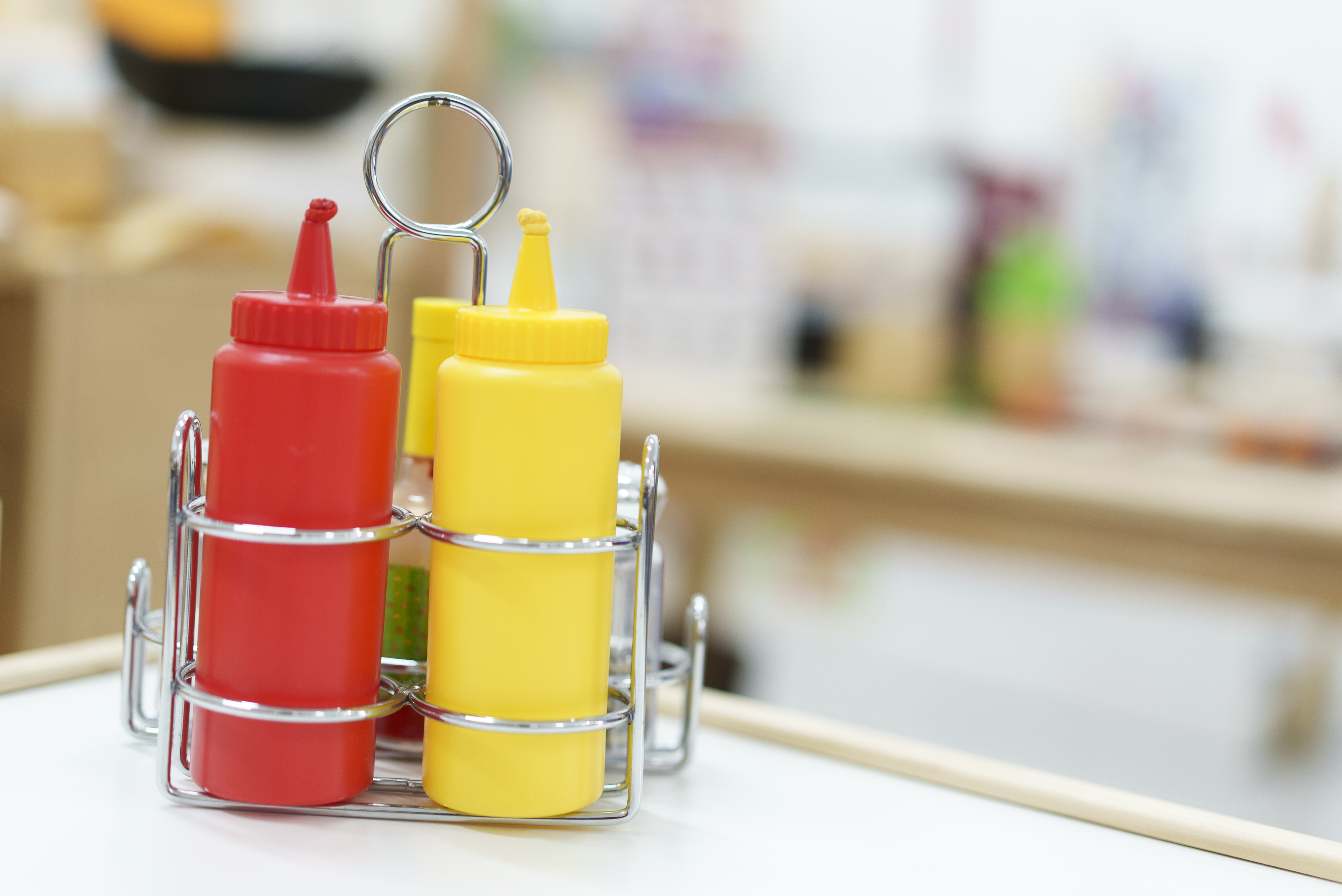 Condiment bottles in a metal holder on a table, with red and yellow squeeze bottles for sauces