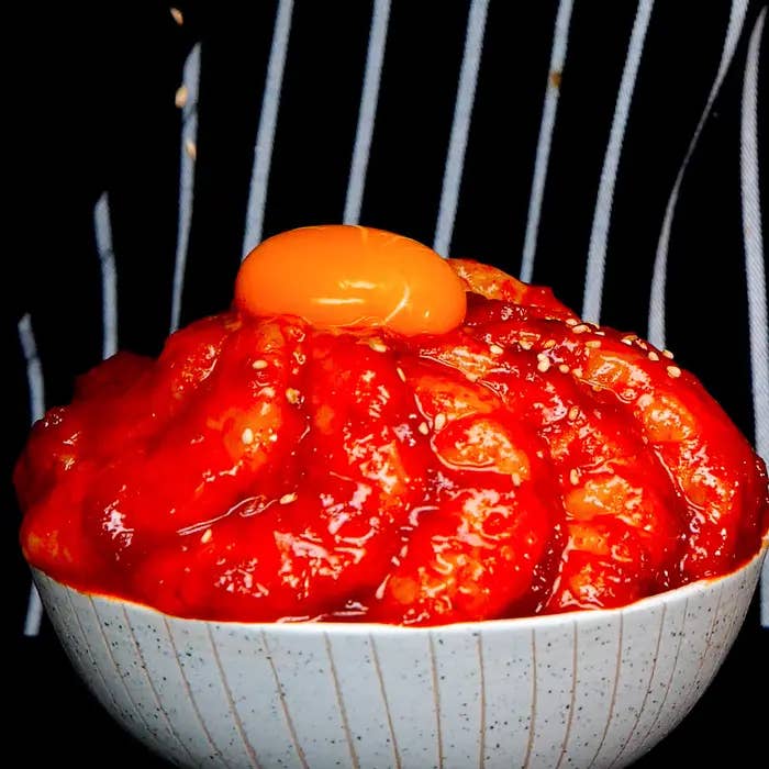 白い陶器のボウルに盛られた辛そうなソースをかけた韓国料理。卵黄が上にのっている。