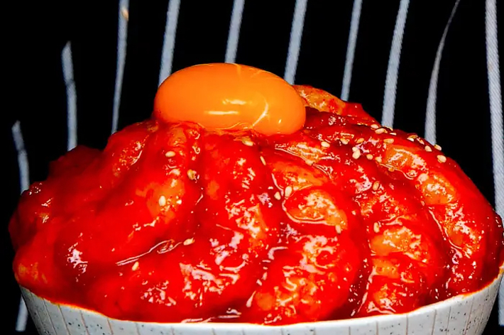 卵黄が載ったピリ辛ソースをかけた料理の写真。ボウルに盛られた料理が中心に映し出されています。