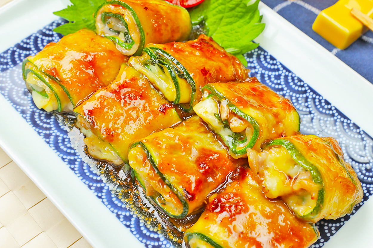 お皿に盛り付けられたズッキーニとチーズの巻物料理。上にはソースがかかっており、トマトのスライスと葉が添えられている。