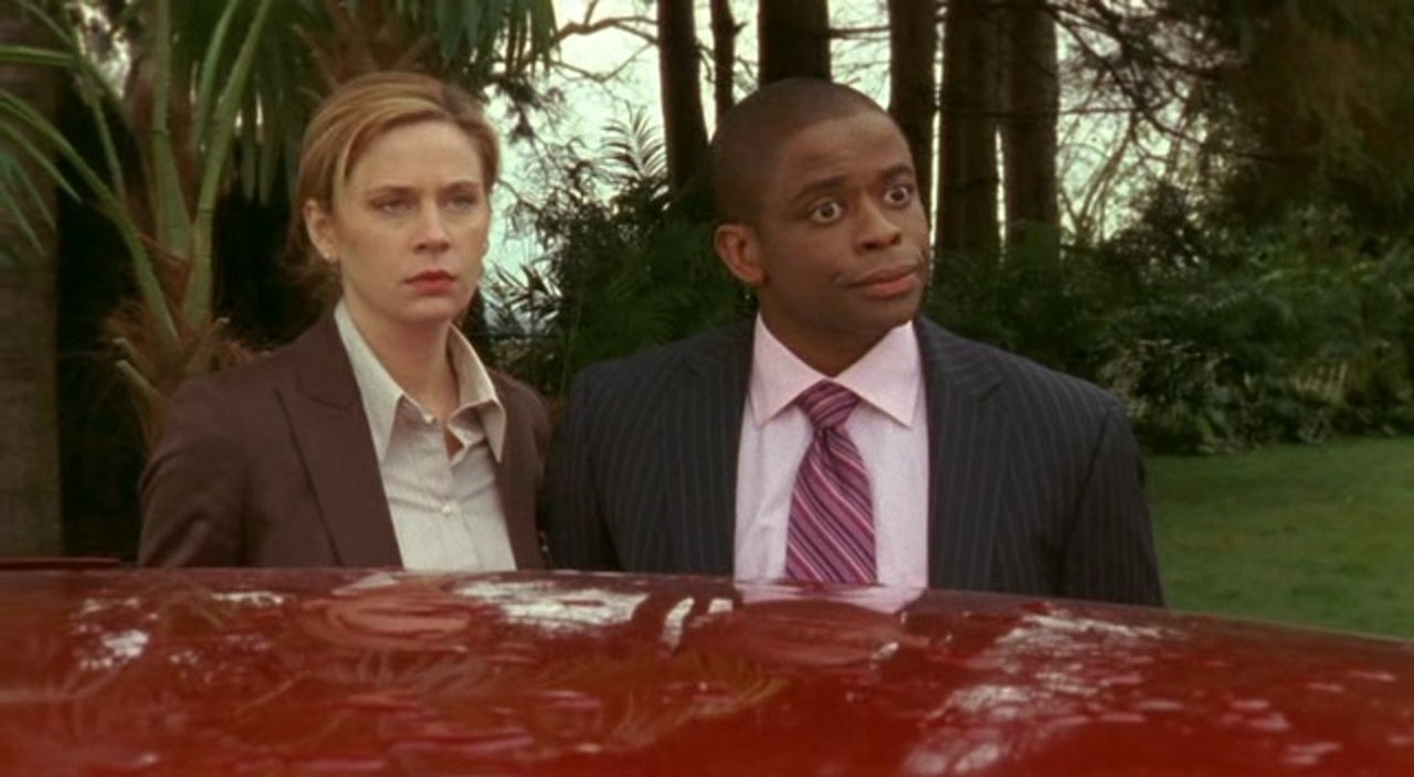Anne Dudek and Dulé Hill in a scene from the TV show "Psych," standing outdoors with a forested background