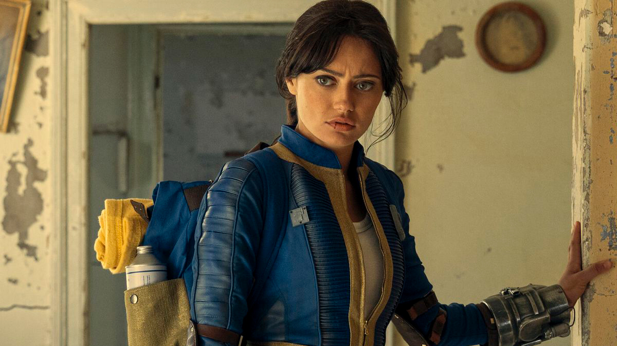 Woman dressed in futuristic, combat-style attire with metal arm gear, standing in a distressed room, holding onto a door frame