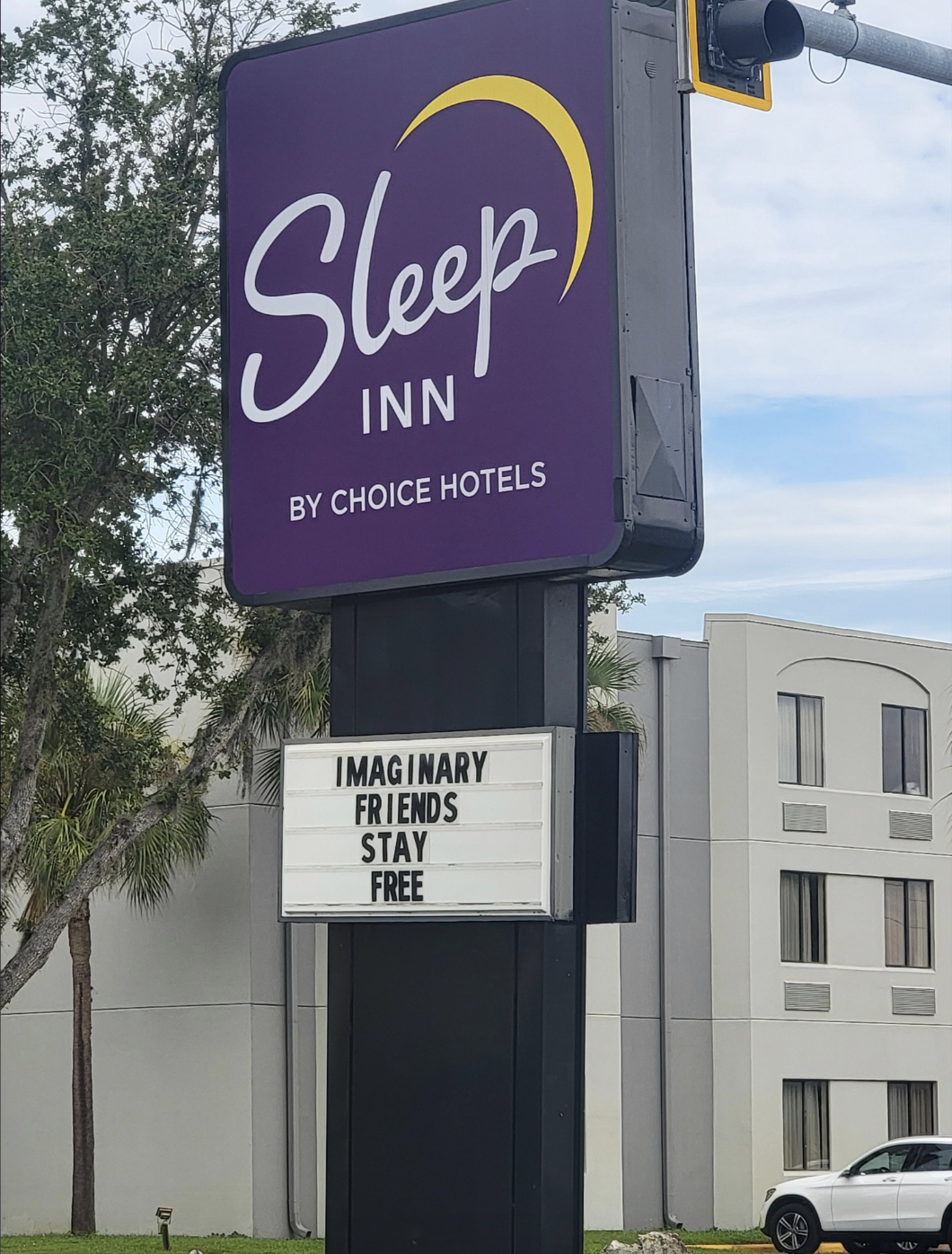 Sleep Inn hotel sign that reads, "Imaginary Friends Stay Free," with a background of the hotel building and some trees