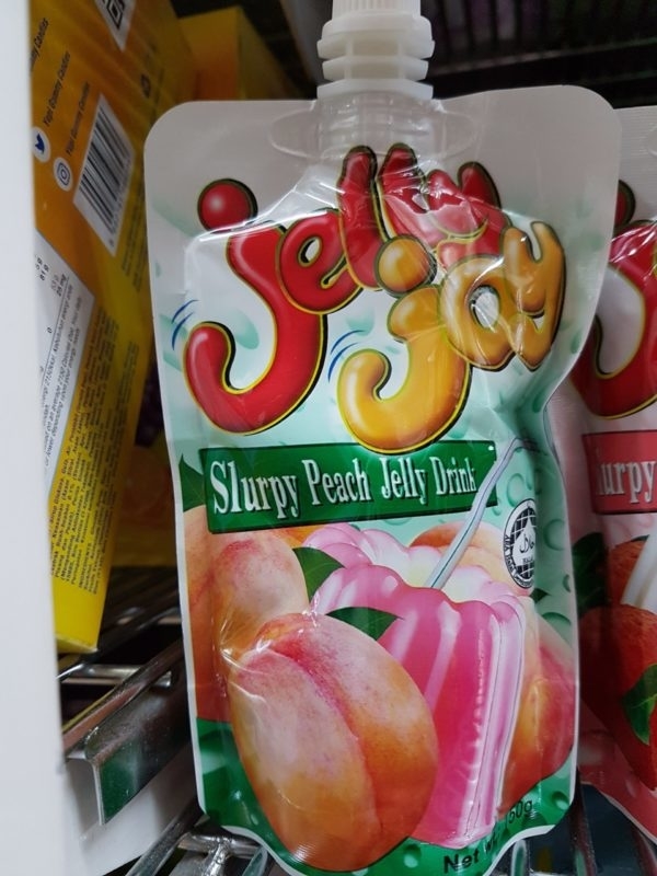 Jelly Joy Slurpy Peach Jelly Drink pouch on a store shelf. The package features images of peaches and a pink jelly drink