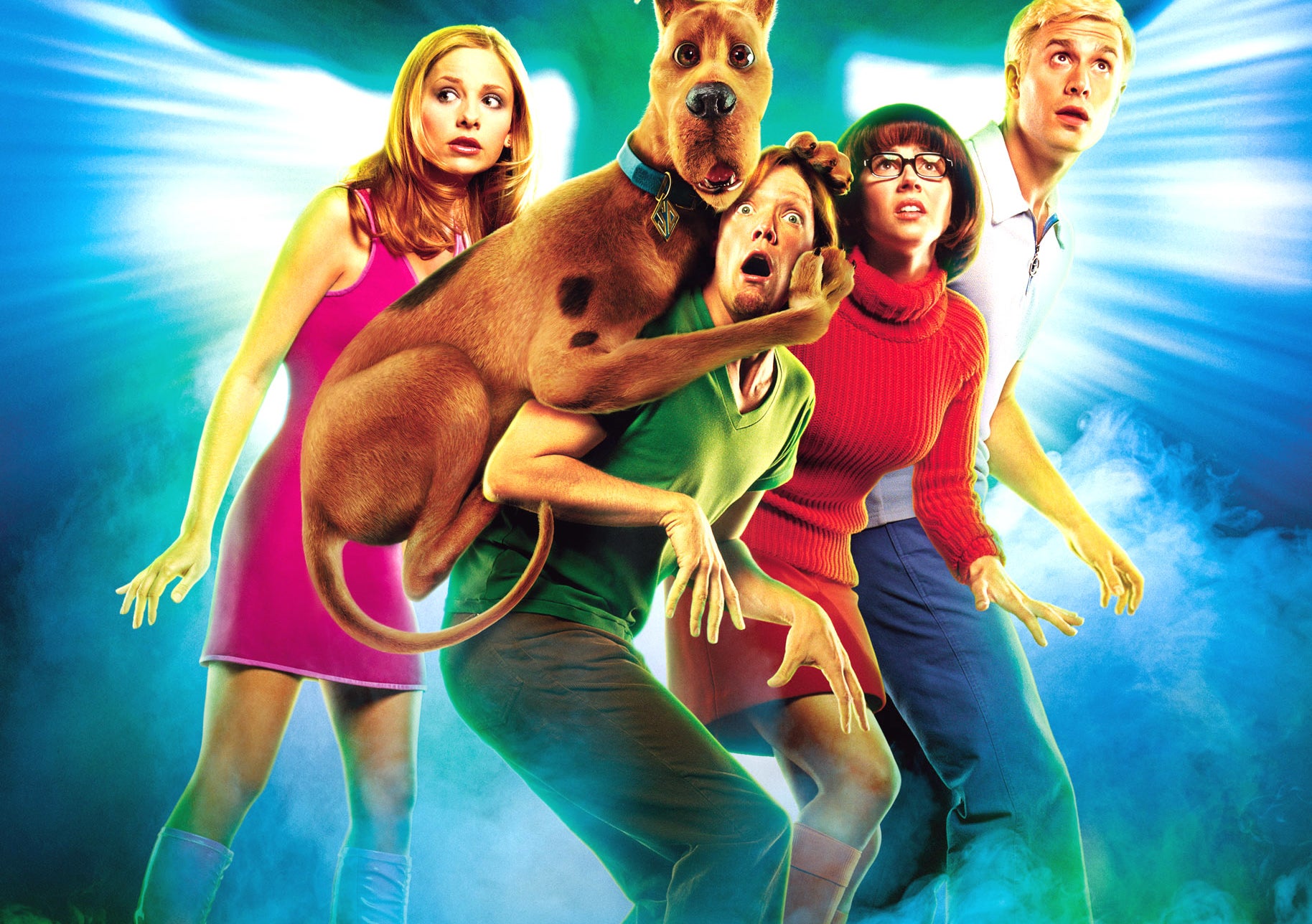Sarah Michelle Gellar, Freddie Prinze Jr., Linda Cardellini, Matthew Lillard, and Scooby-Doo in a spooky, dramatic pose with a ghostly figure behind them