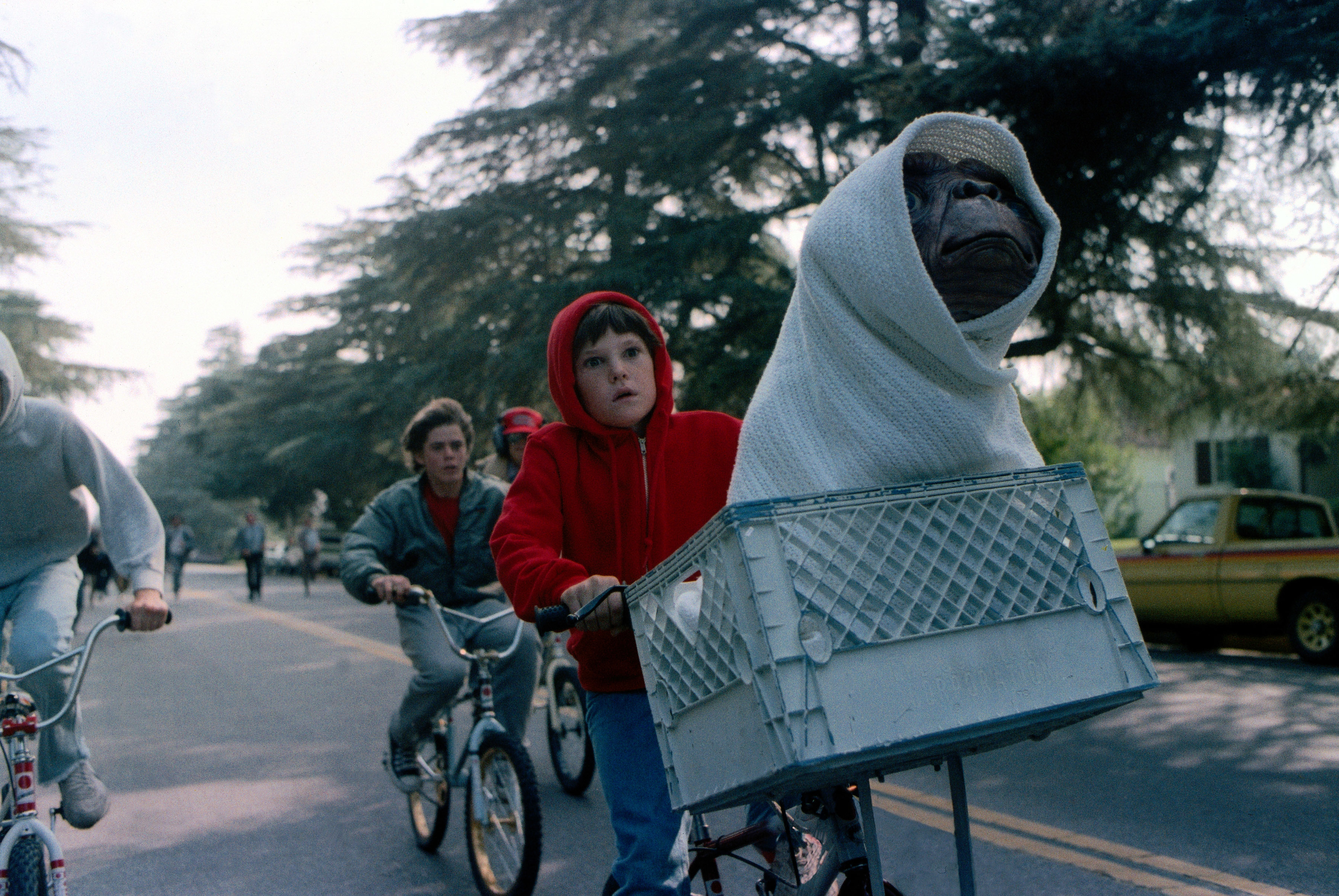 Henry Thomas rides a bicycle with E.T. in a basket wrapped in a blanket, alongside other cyclists in a scene from the movie &quot;E.T. the Extra-Terrestrial&quot;