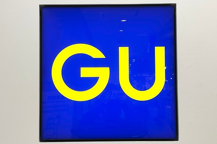 A square sign with the bright yellow letters &ldquo;GU&rdquo; on a blue background