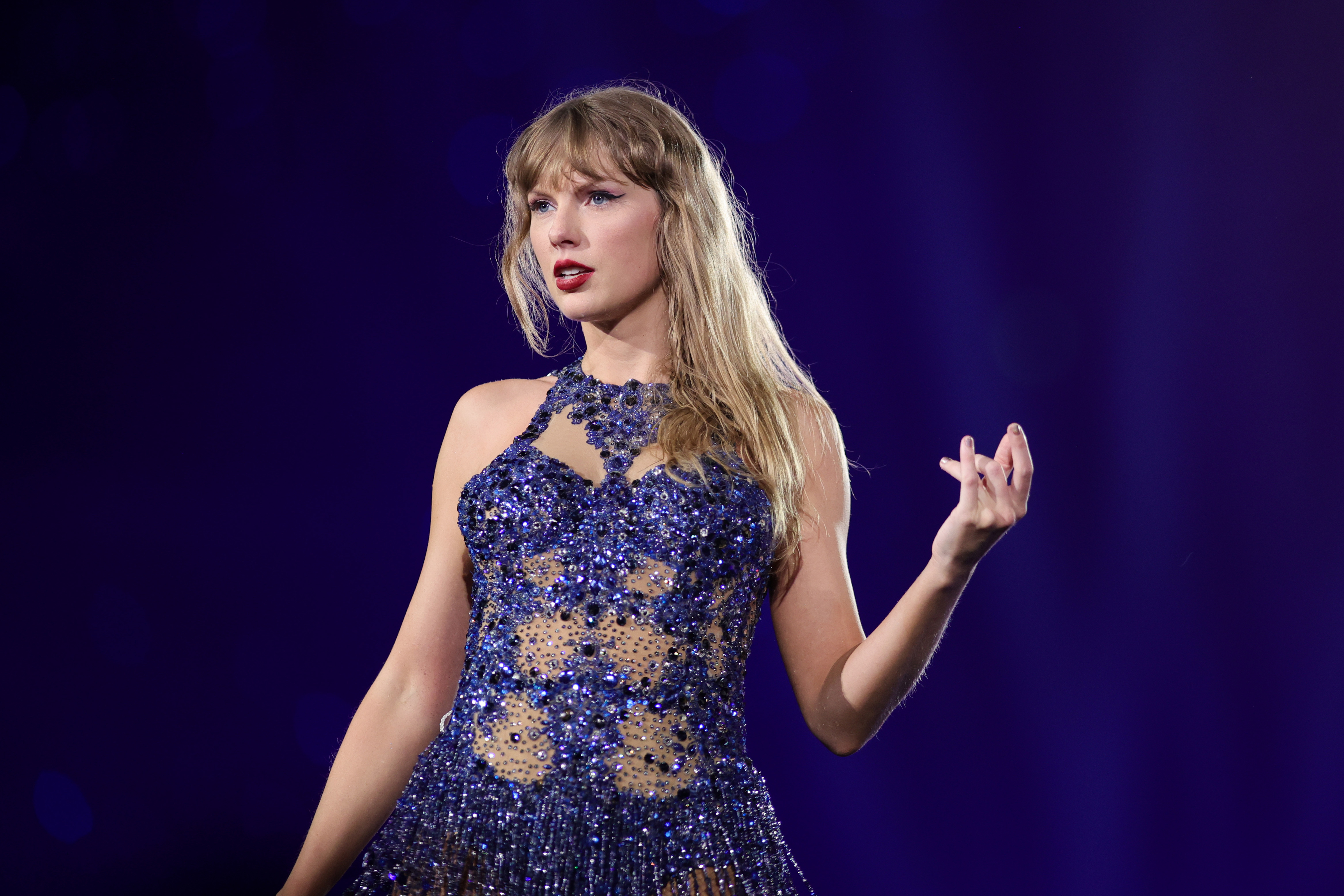 Taylor Swift wearing a sparkly, sleeveless gown performs onstage