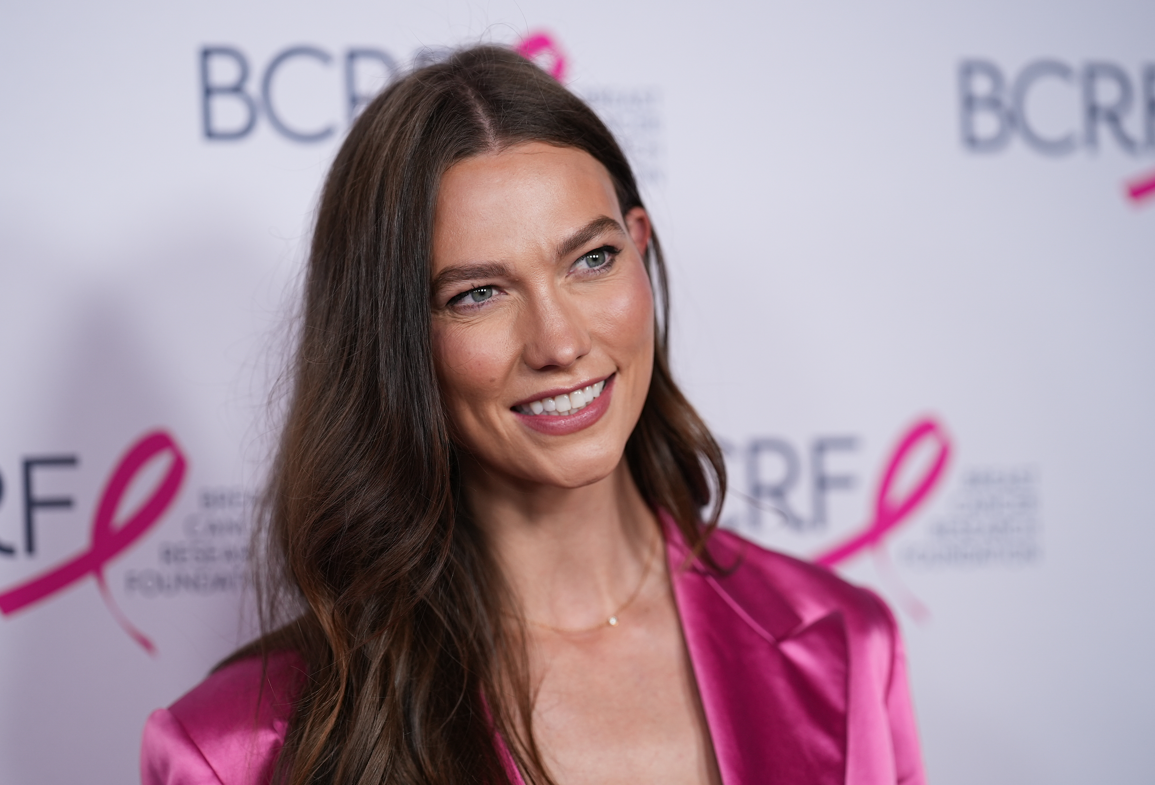Karlie Kloss at the Breast Cancer Research Foundation (BCRF) event, wearing a stylish, shiny blazer. She is smiling at the camera