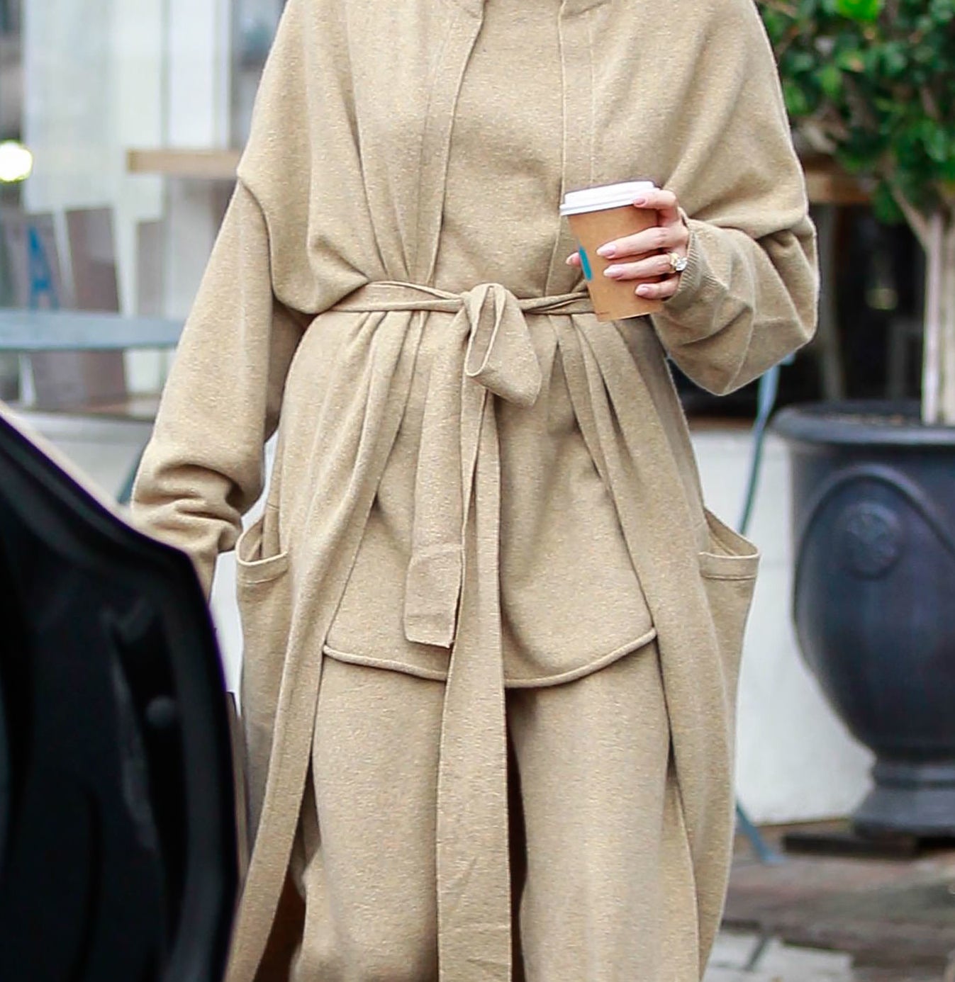 Hailey Bieber steps out in a casual, oversized beige outfit, holding a coffee cup and wearing sunglasses, while walking on a sidewalk