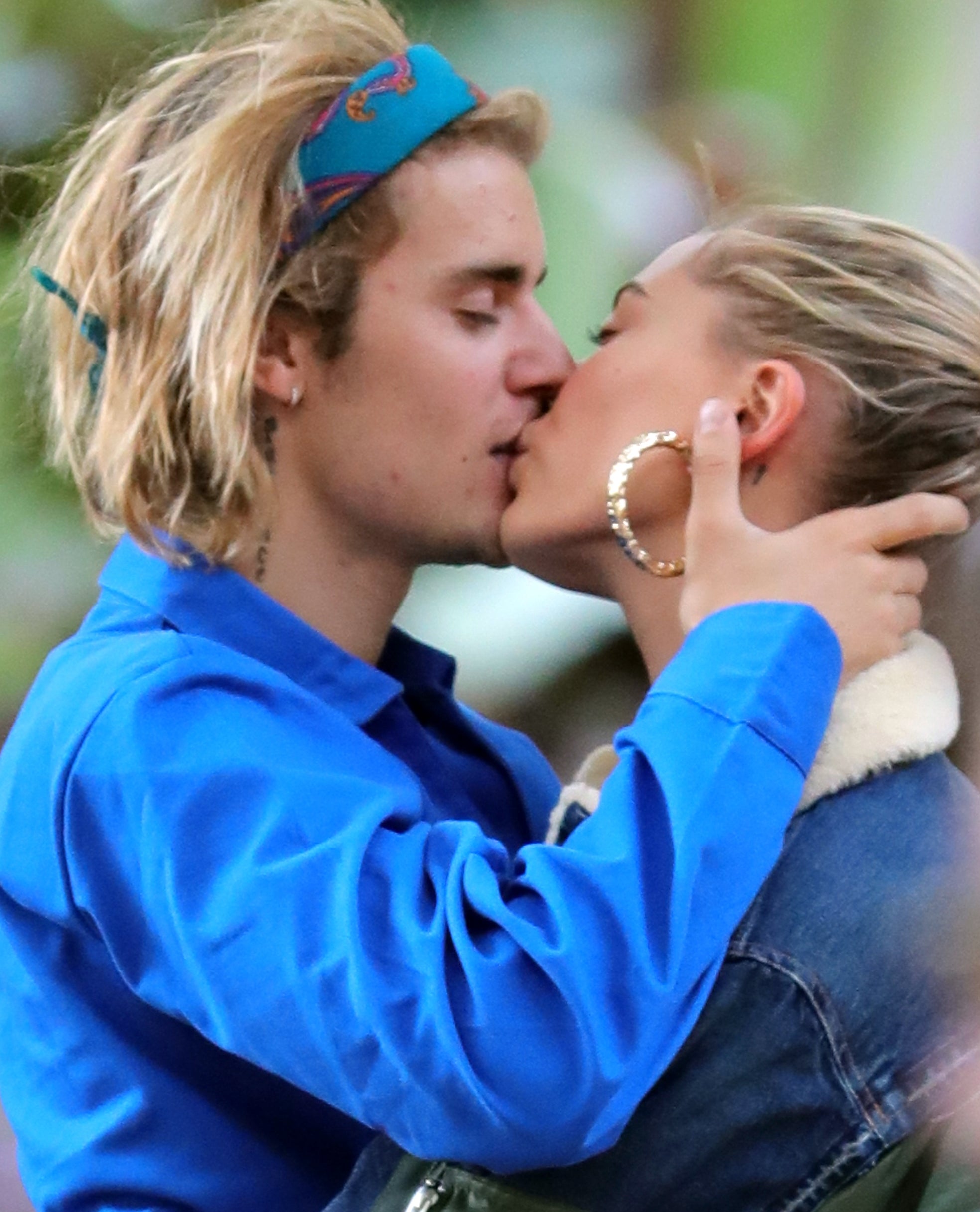 Justin Bieber and Hailey Baldwin share a kiss, with Justin wearing a headband and a jacket, and Hailey in hoop earrings and a denim jacket