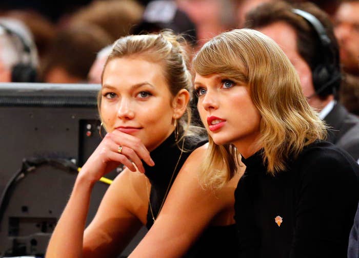 Karlie Kloss and Taylor Swift sitting together attentively watching something off-camera at a public event