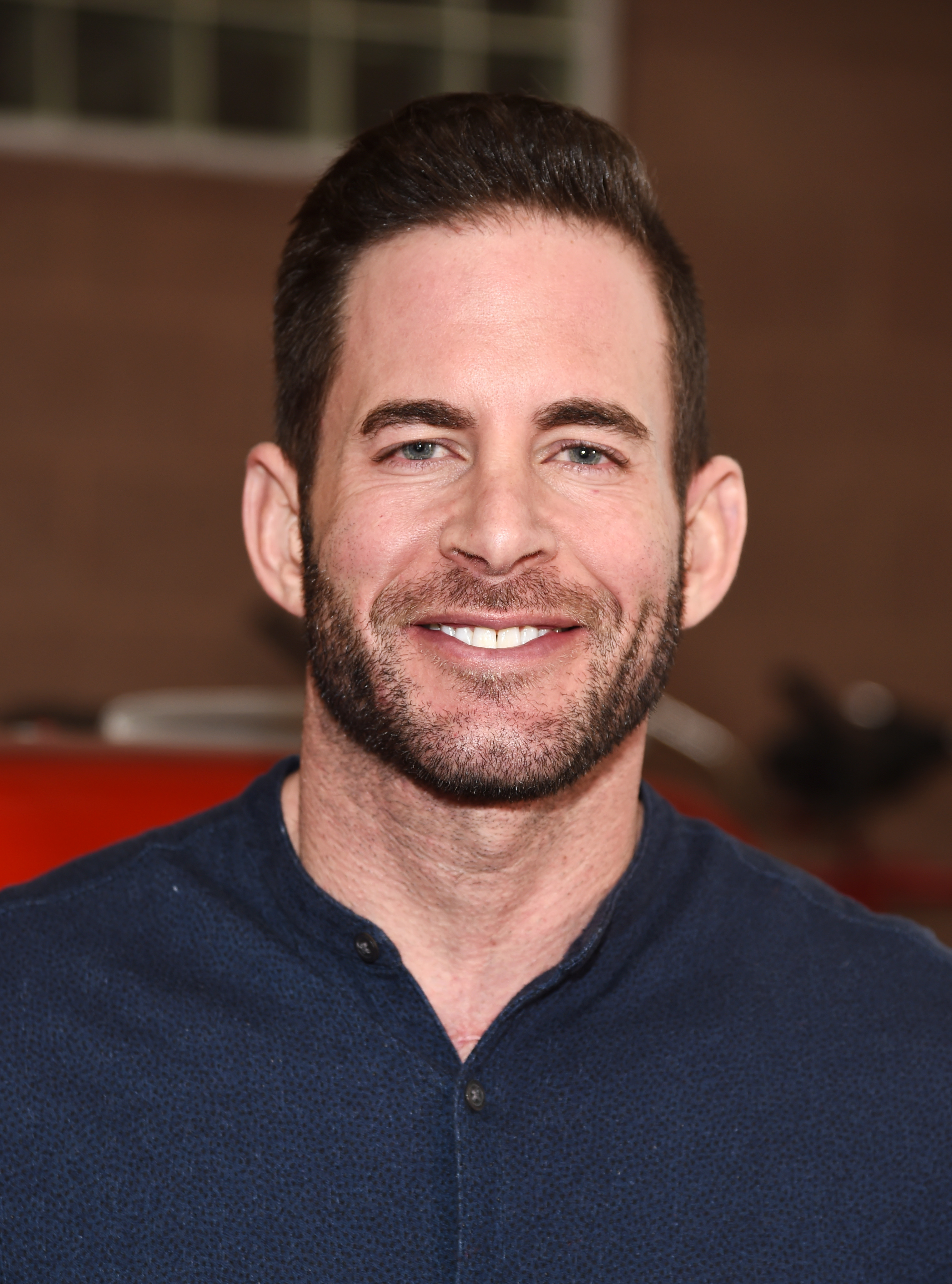 Tarek El Moussa smiling at a camera, wearing a casual blue shirt