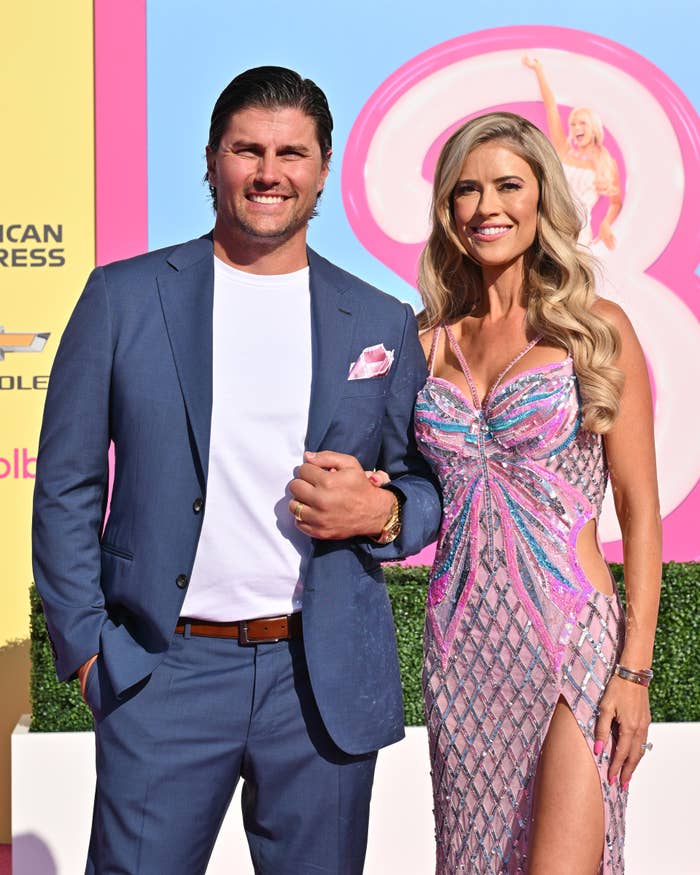 Josh Hall and Christina Hall on the red carpet. Christina is wearing a sparkling, form-fitting dress with a thigh-high slit, holding Josh's arm