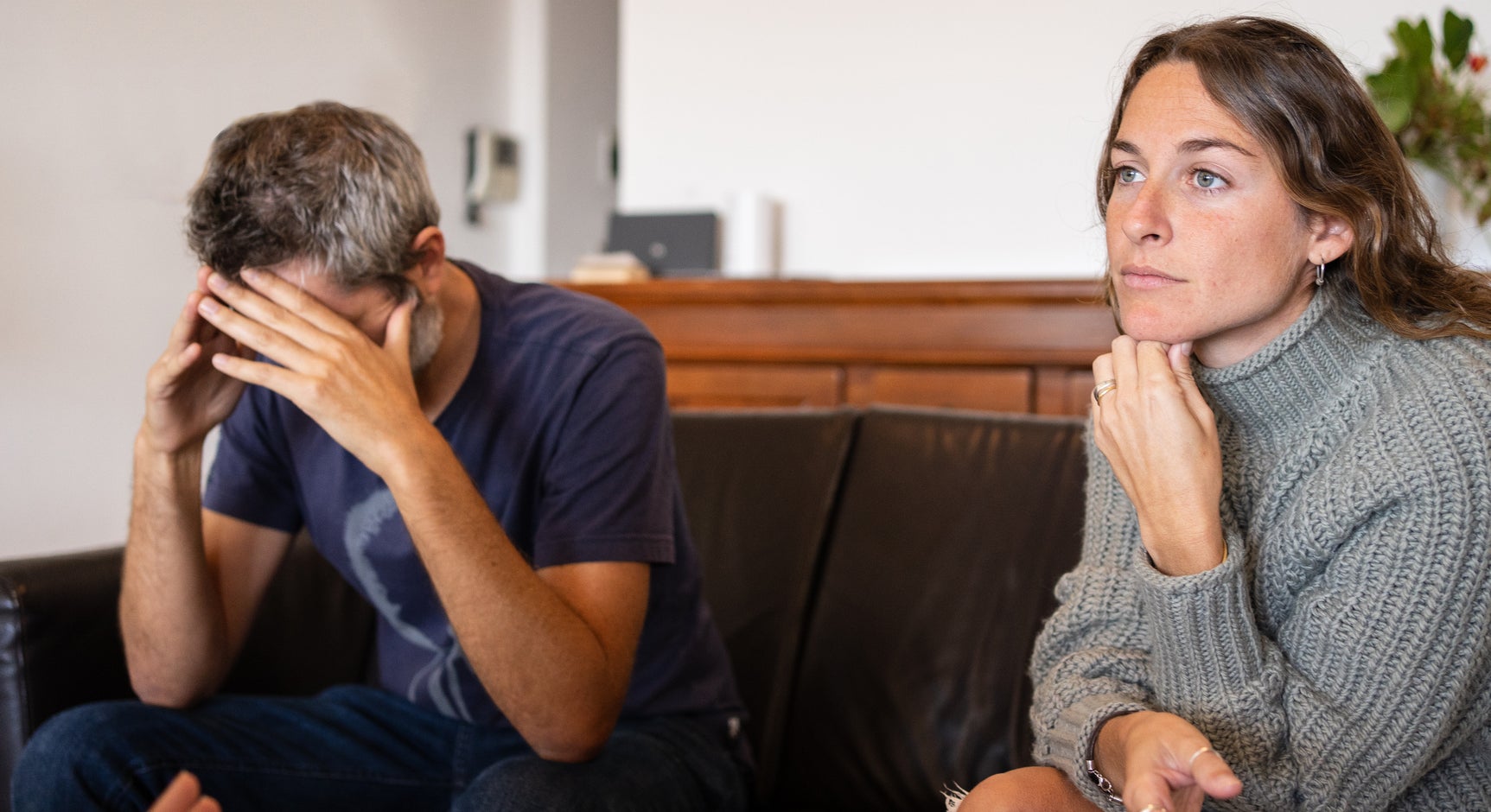 A couple sitting on a couch, the man with his head in his hands and the woman looking thoughtful, during a conversation with an unseen person