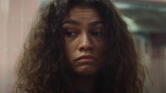 Zendaya with voluminous, curly hair, looking slightly to the side with a neutral expression