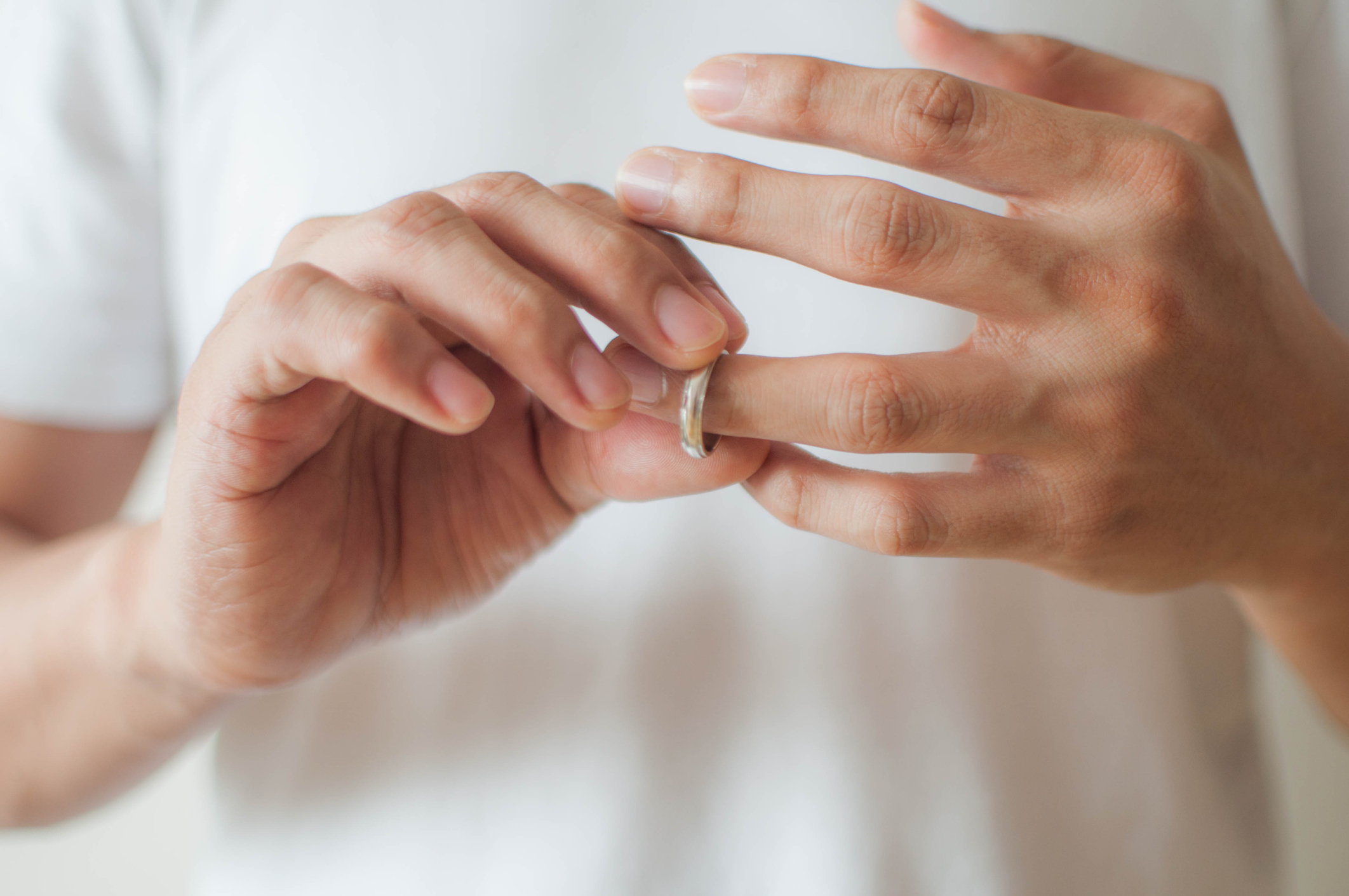 A person slowly removes a wedding ring from their finger, symbolizing the end of a relationship. Their expression is not visible