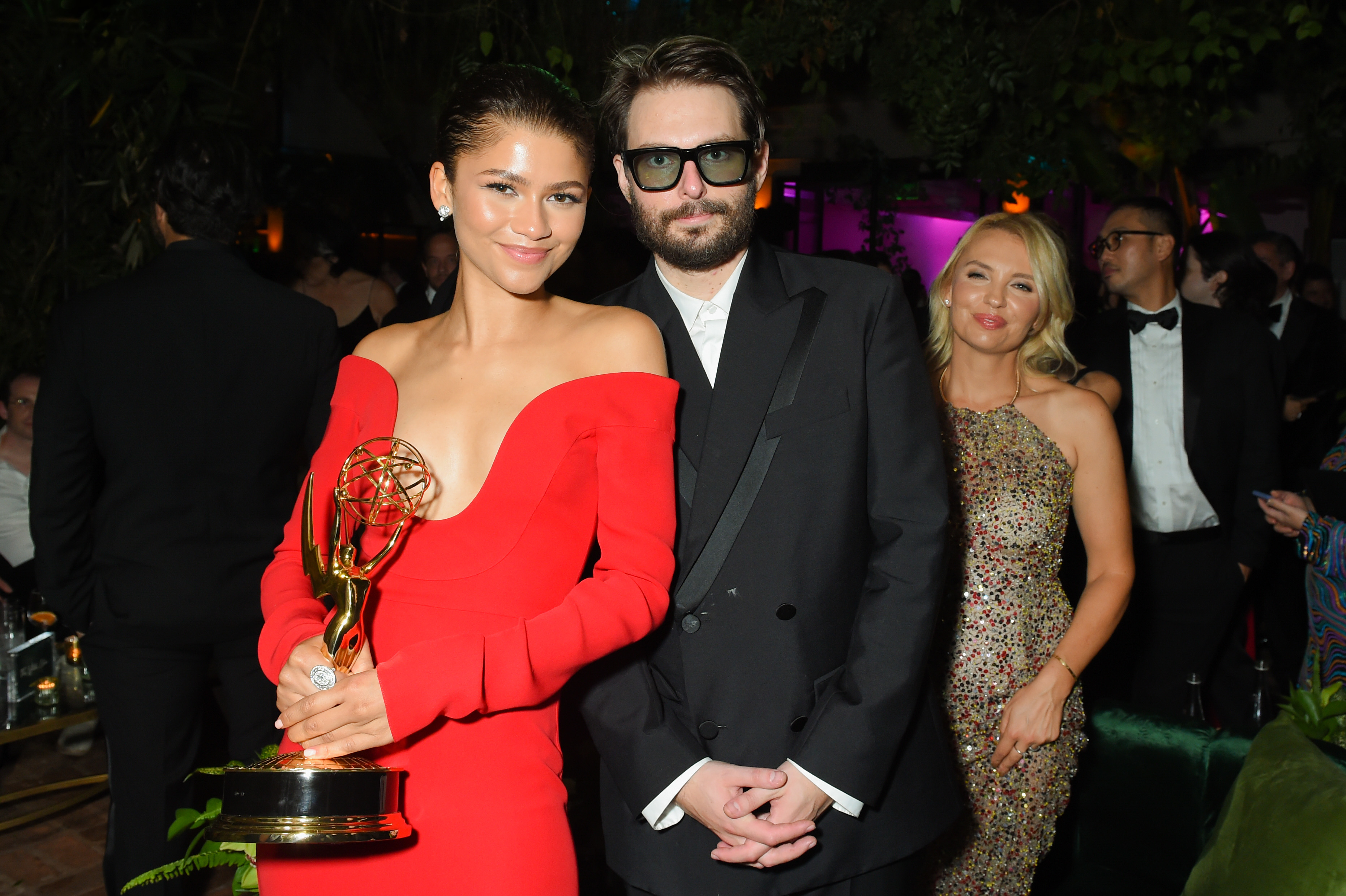 Zendaya holds an Emmy award in an off-the-shoulder dress next to Sam