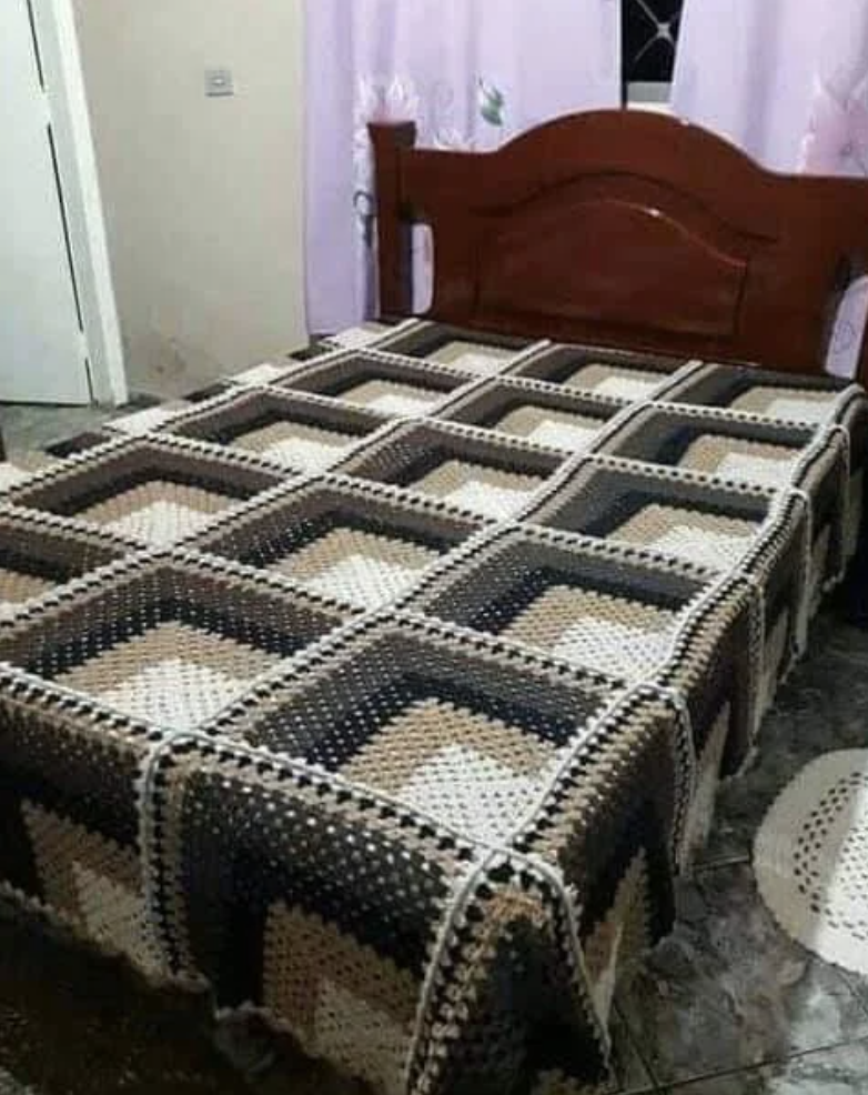A neatly made bed with a geometric-patterned crocheted blanket covering it, set in a simple bedroom with a wooden headboard and tiled floor