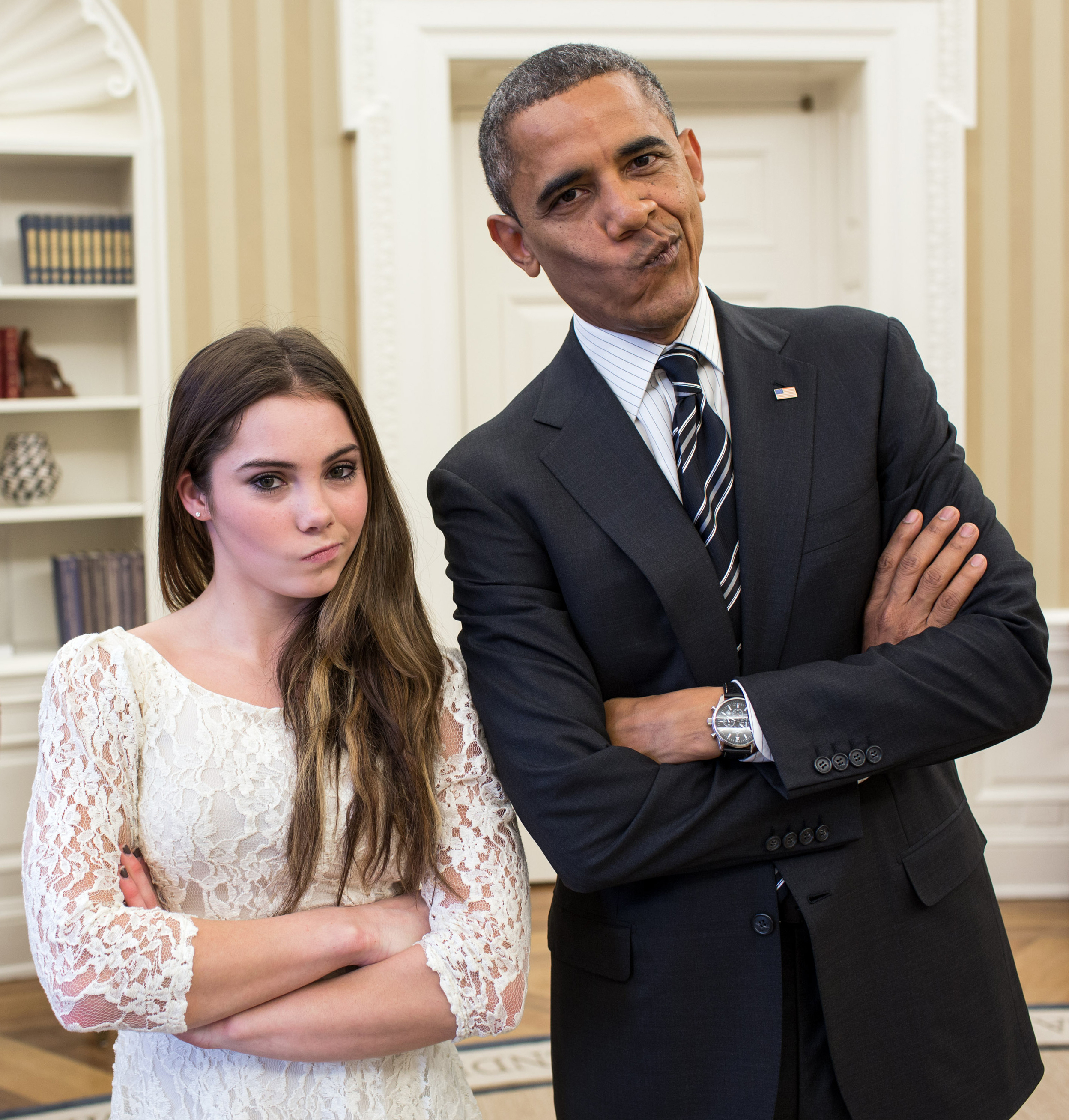 Barack Obama in a dark suit with a striped tie and McKayla Maroney in a white lace dress both pose with arms crossed and slight smirks
