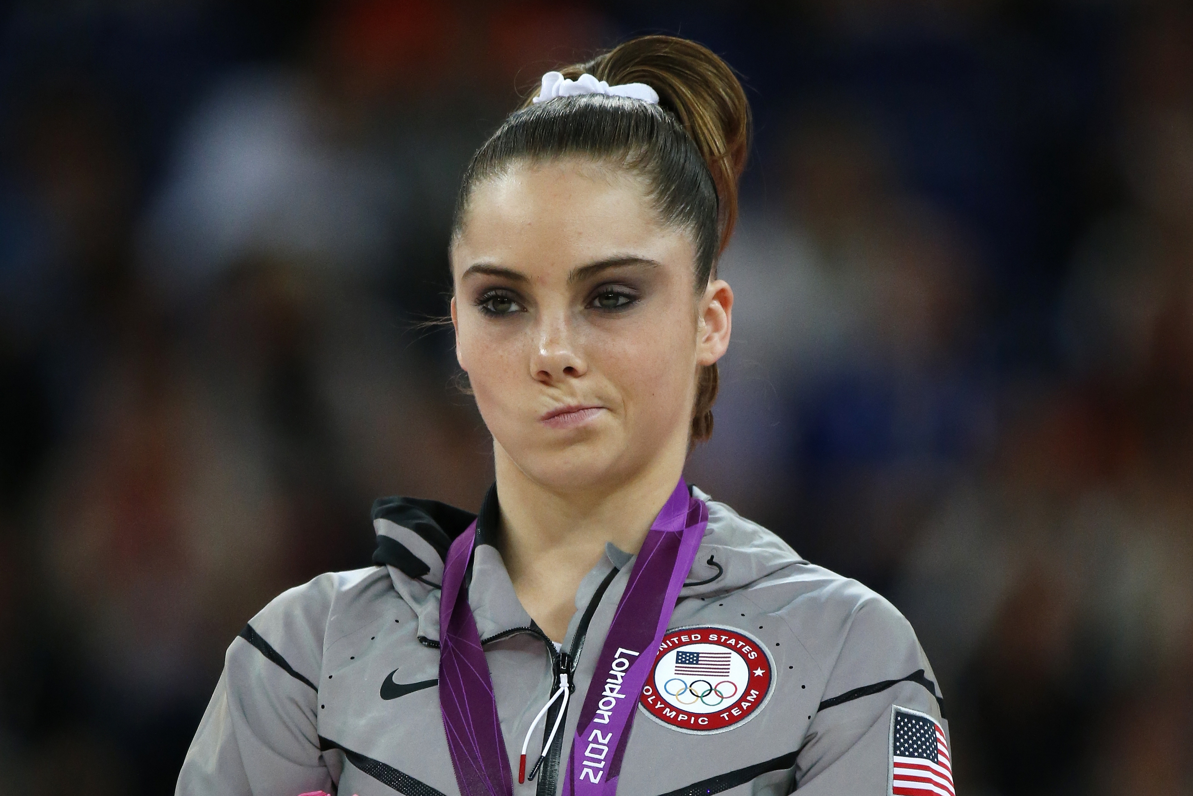 McKayla Maroney on the podium wearing an Olympic jacket with a skeptical expression, silver medal around her neck, London 2012