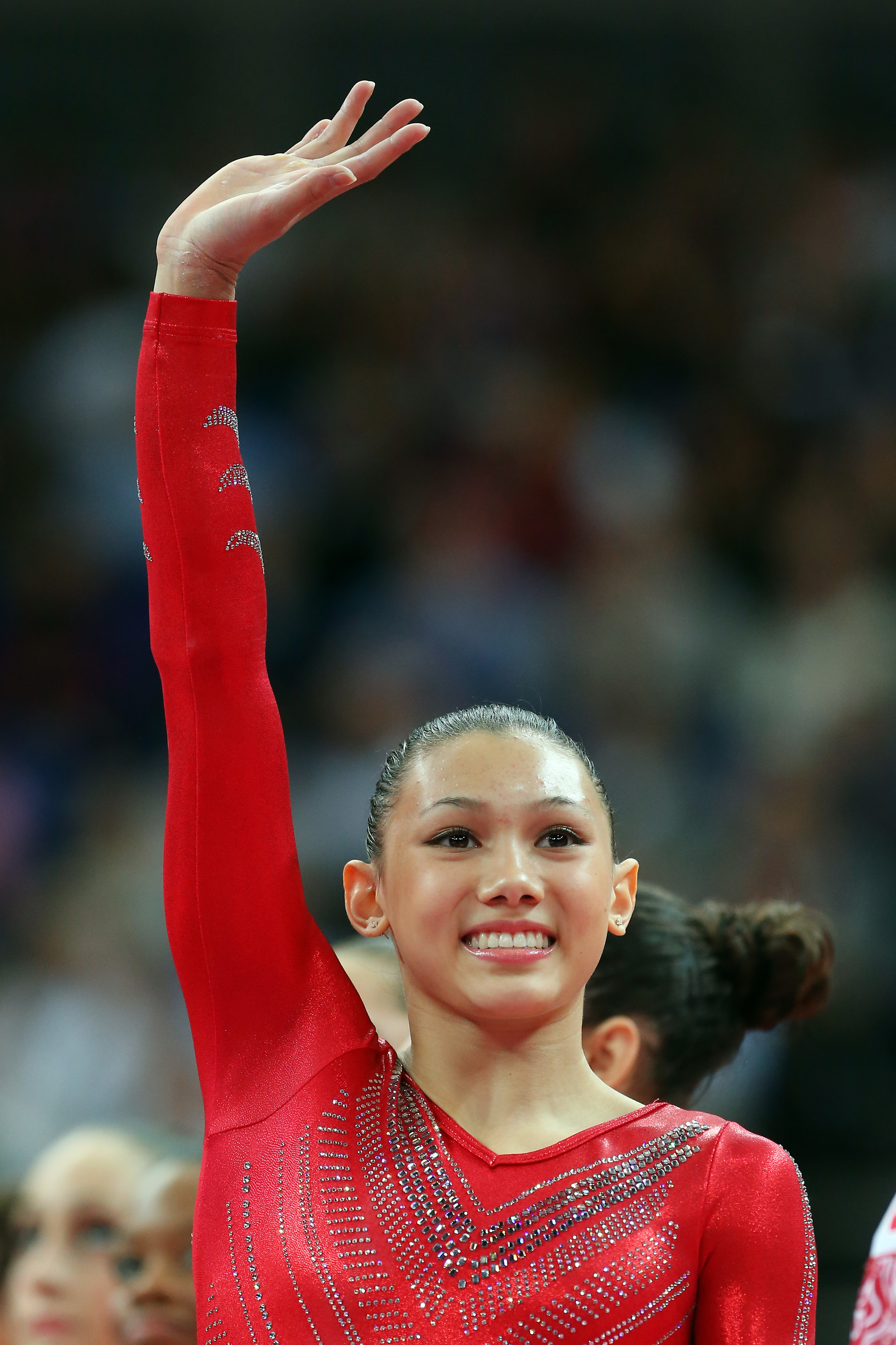 Gymnast Kyla Ross waves, dressed in an embellished long-sleeve leotard, during a competition event