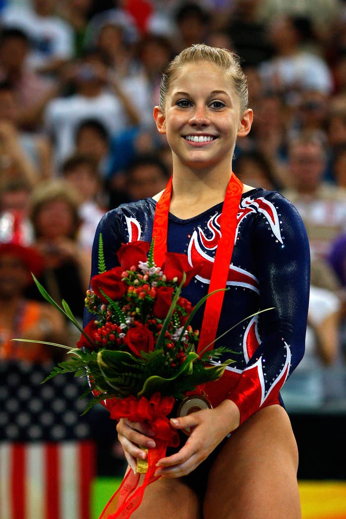 Shawn Johnson smiles while holding a bouquet of roses, wearing a gymnast leotard with a medal around her neck