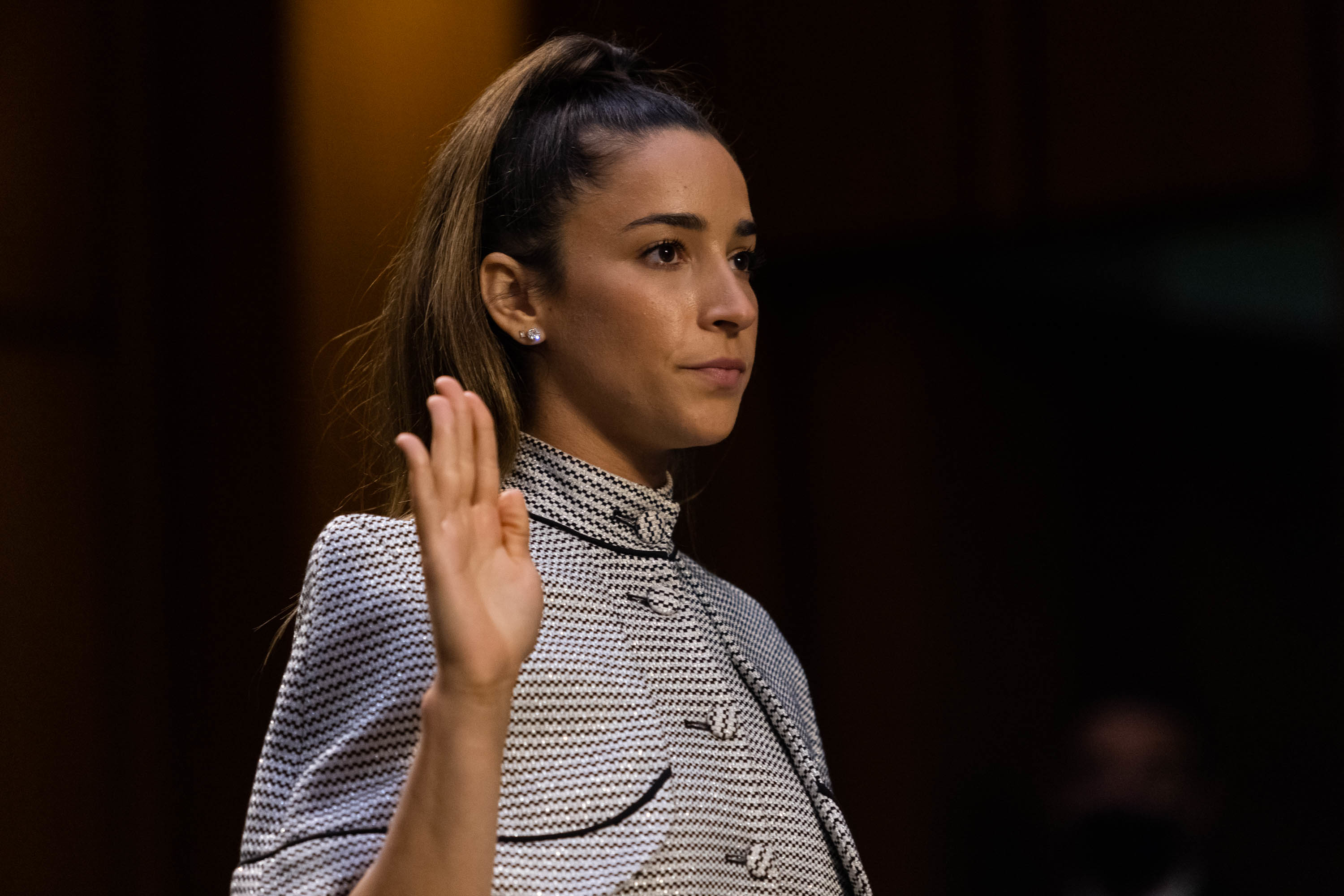 Aly Raisman testifies in a patterned outfit, raising her right hand