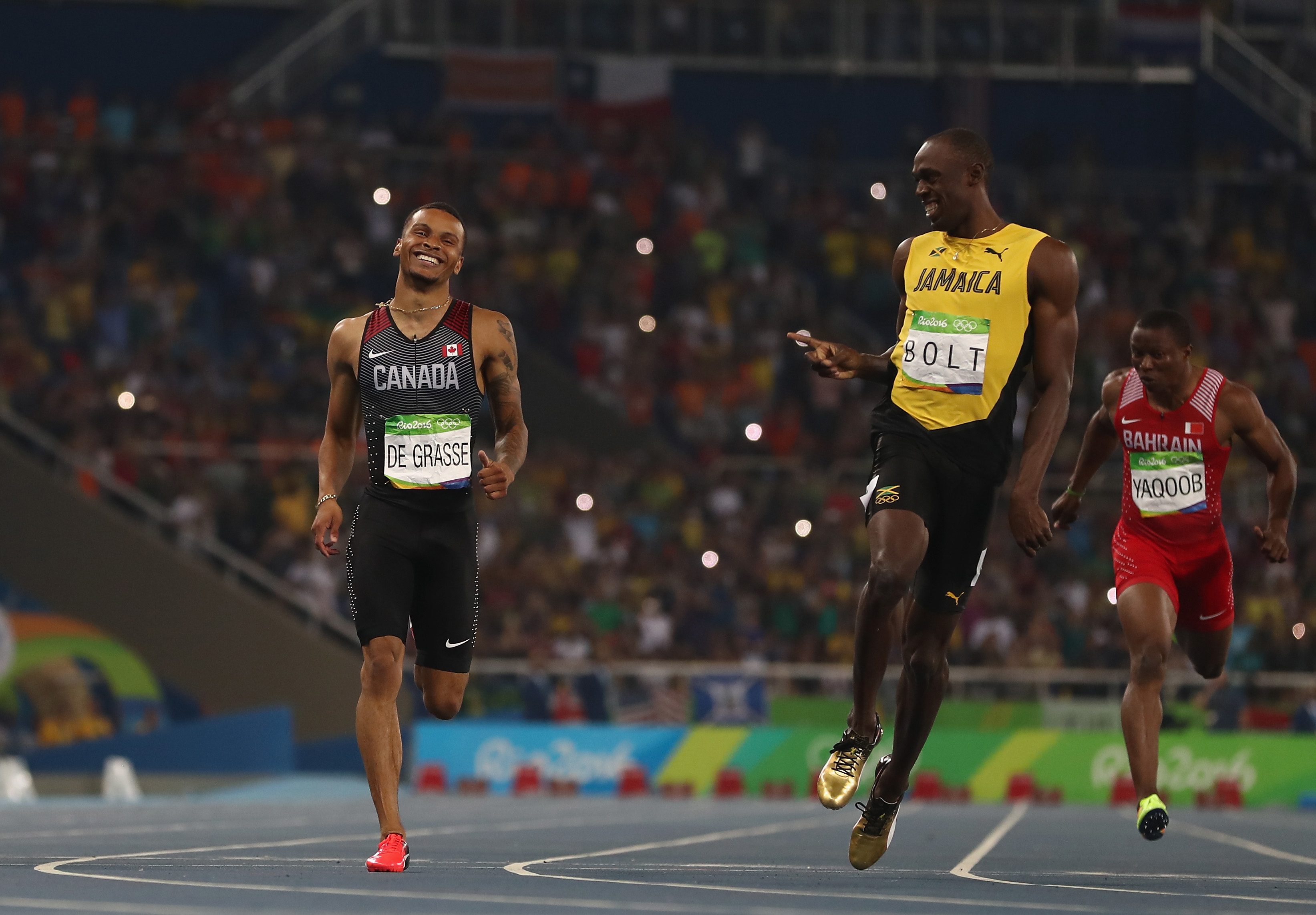 Andre De Grasse, Usain Bolt, and Abdul Hakim Sani Brown running in a track event, with De Grasse and Bolt smiling at each other mid-race