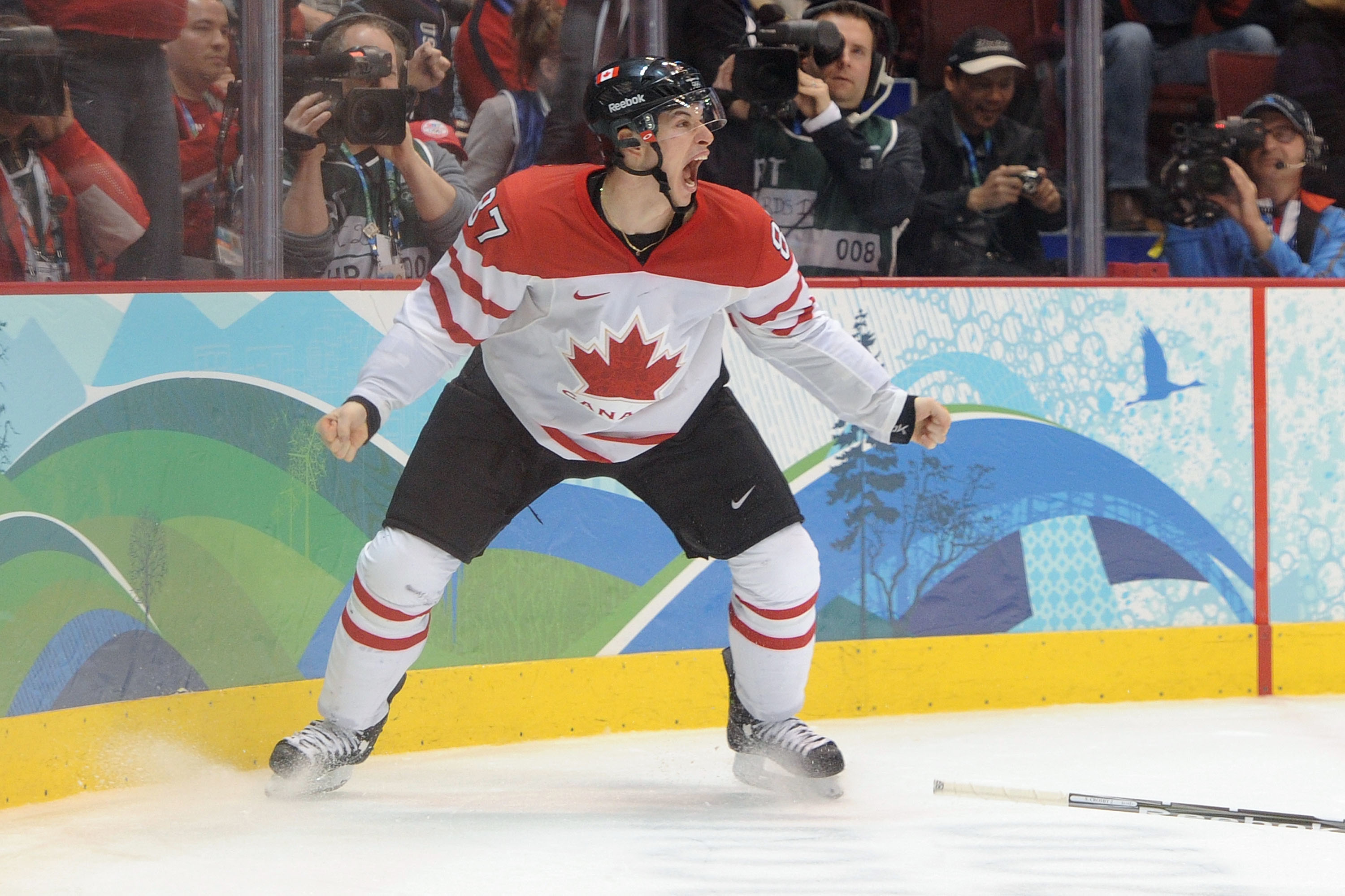 A hockey player in a Team Canada jersey celebrates on the ice in front of photographers